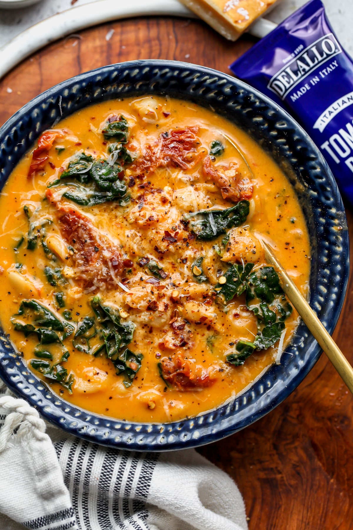 A bowl of Tuscan Butter Bean Soup styled next to DeLallo tomsto paste on a wooden surface.