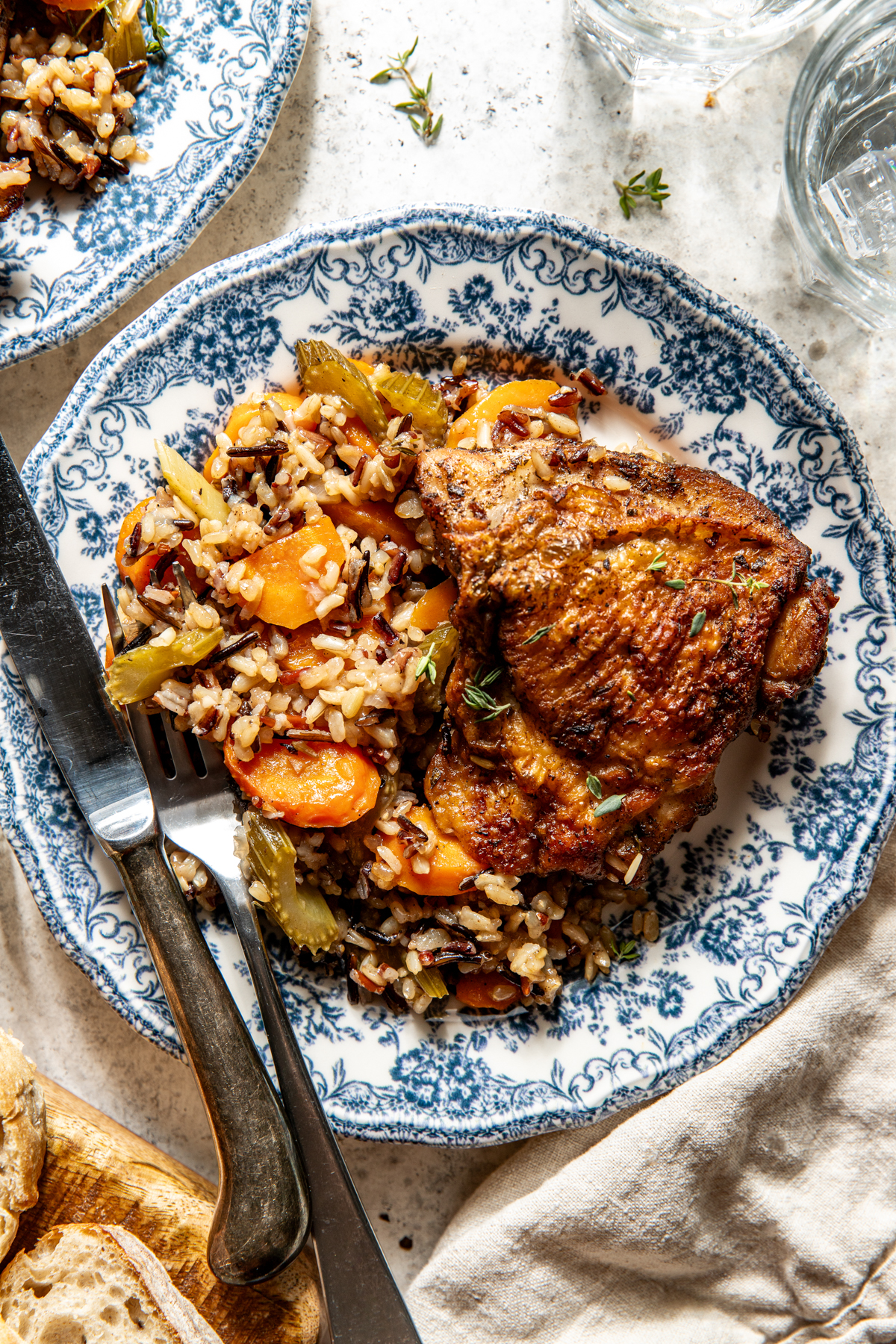 One chicken thigh with wild rice and veggies styled on a white and blue floral plate.