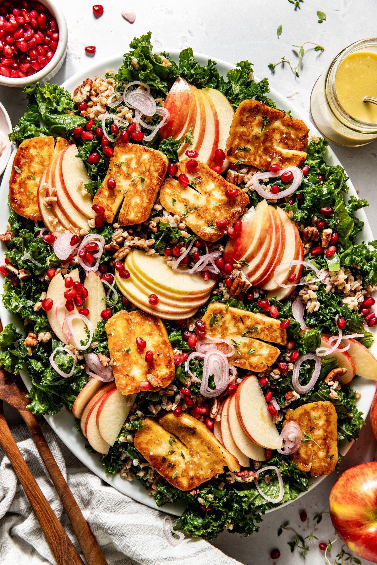 Halloumi salad assembled on a platter topped with apple slices, pomegranate, pecans, and shallots.