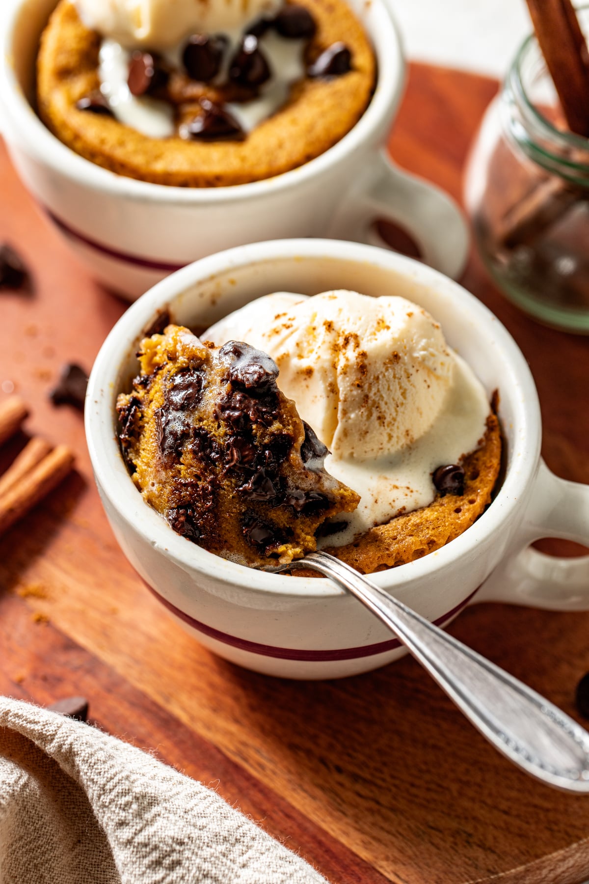 Pumpkin mug cake topped with a scoop of vanilla ice cream styled on a wooden surface with a spoon digging in to show inside texture.