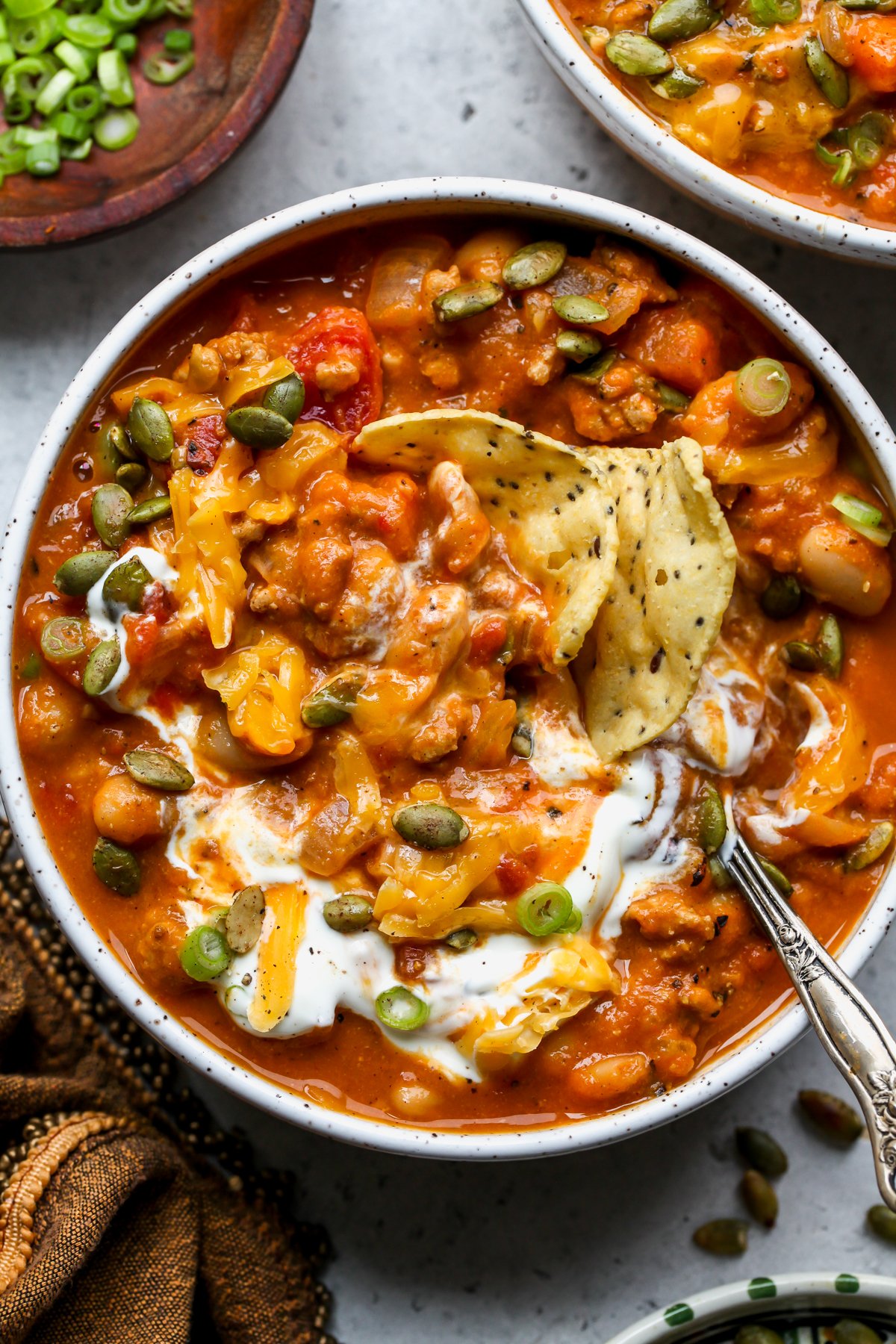 Tortilla chips being dunked into a bowl of turkey pumpkin chili.