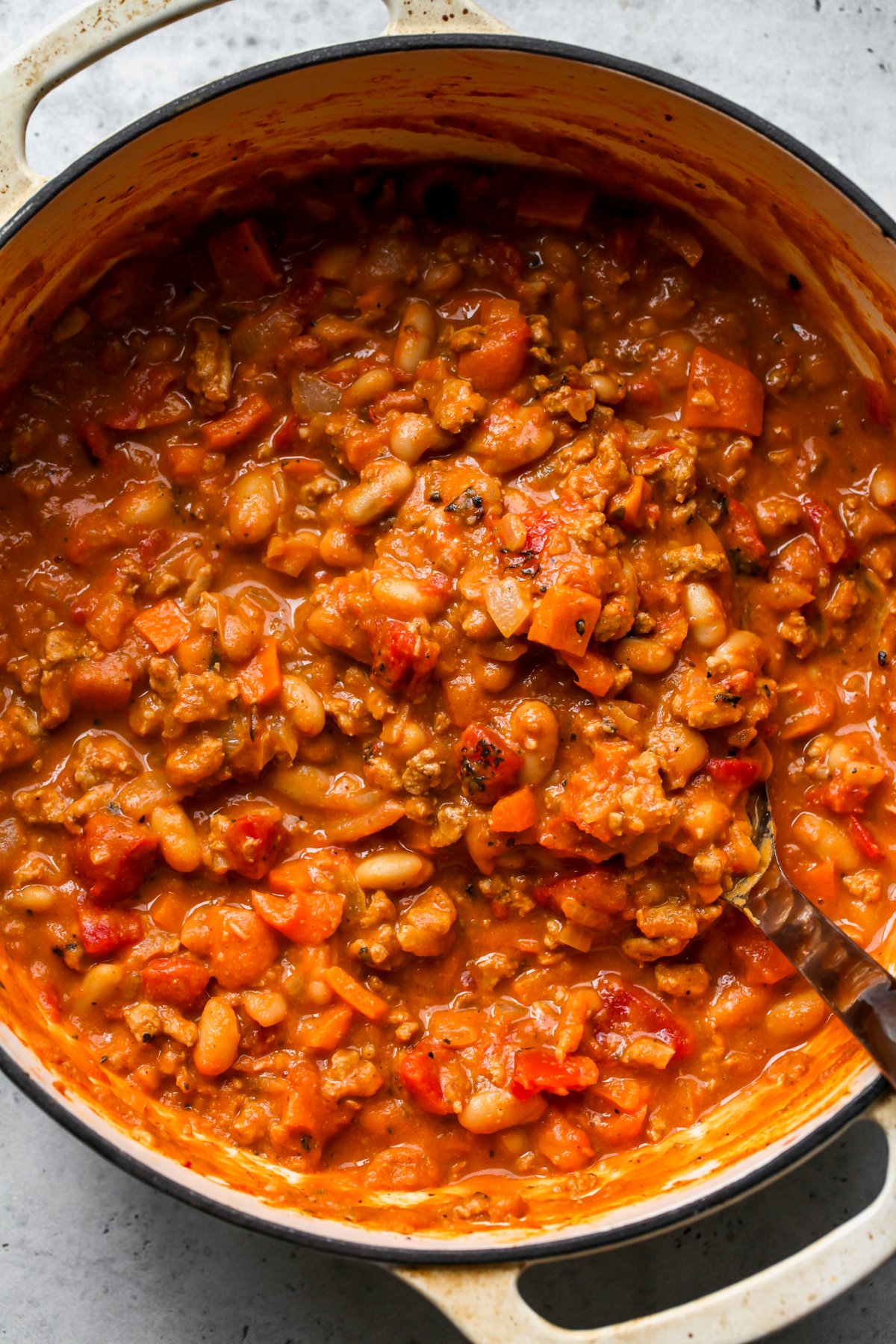 A tan Dutch oven filled with chili being stirred with a ladle.