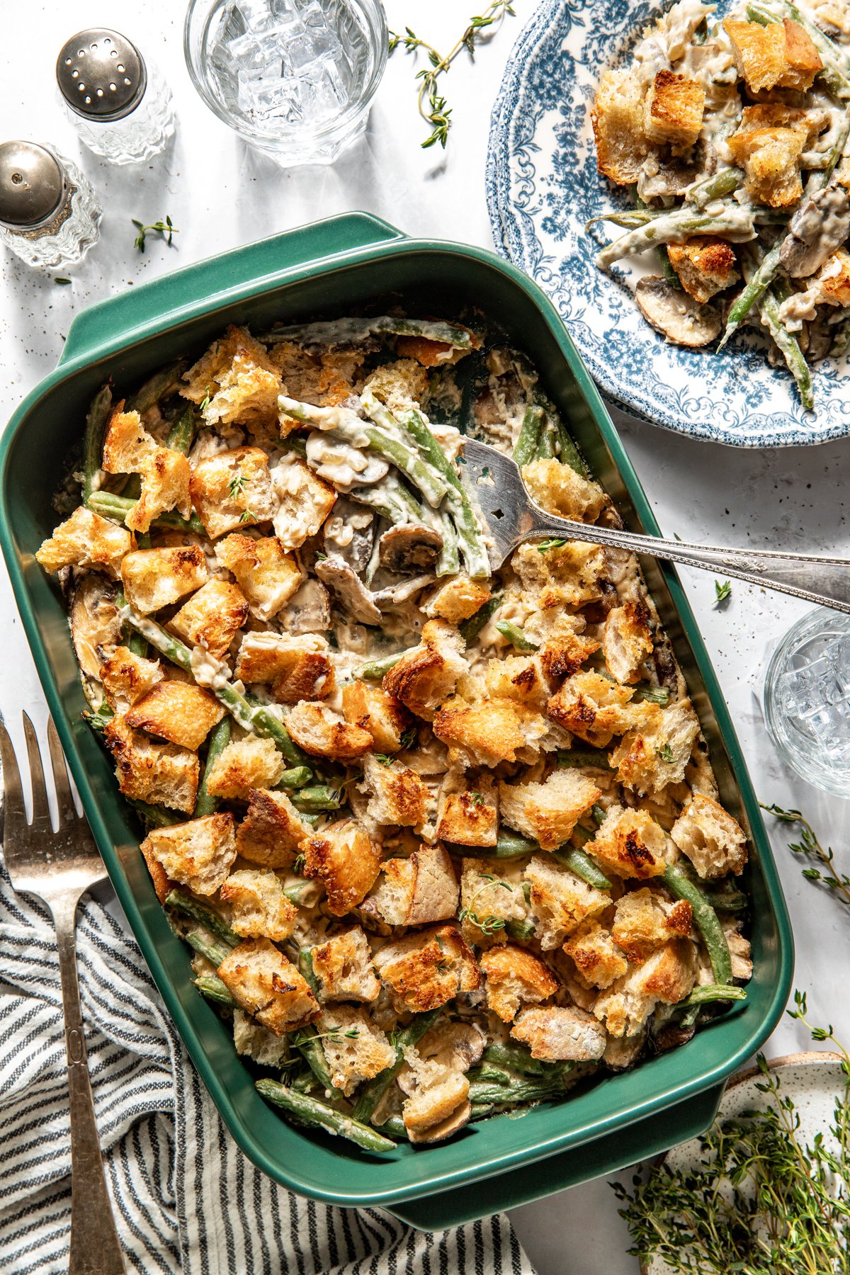 Green bean casserole in a green baking dish styled on a white surface with a serving utensil digging into the upper right corner.
