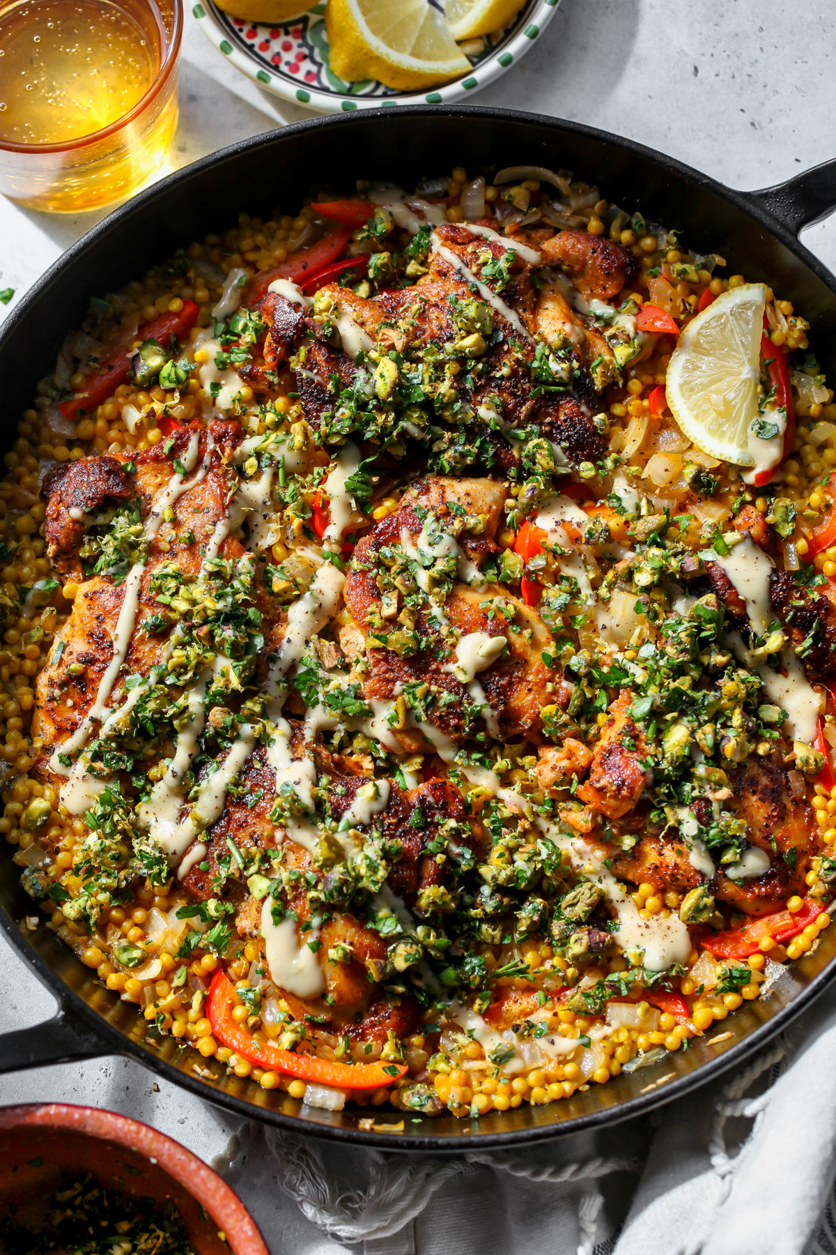 Mediterranean Chicken and Couscous topped with Pistachio Gremolata and Tahini-Honey in a large cast iron skillet.