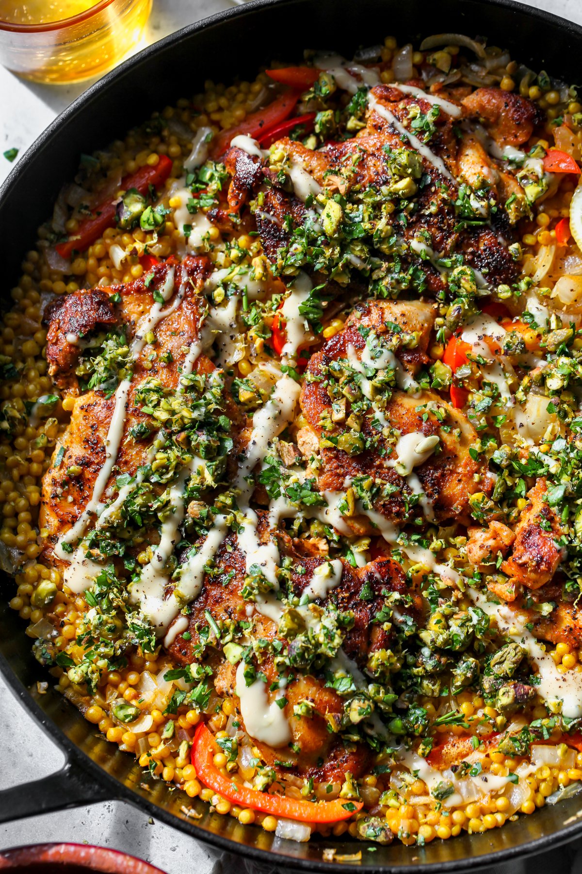 Mediterranean Chicken and Couscous styled in a black cast iron skillet topped with tahini-honey and a pistachio-herb mix.