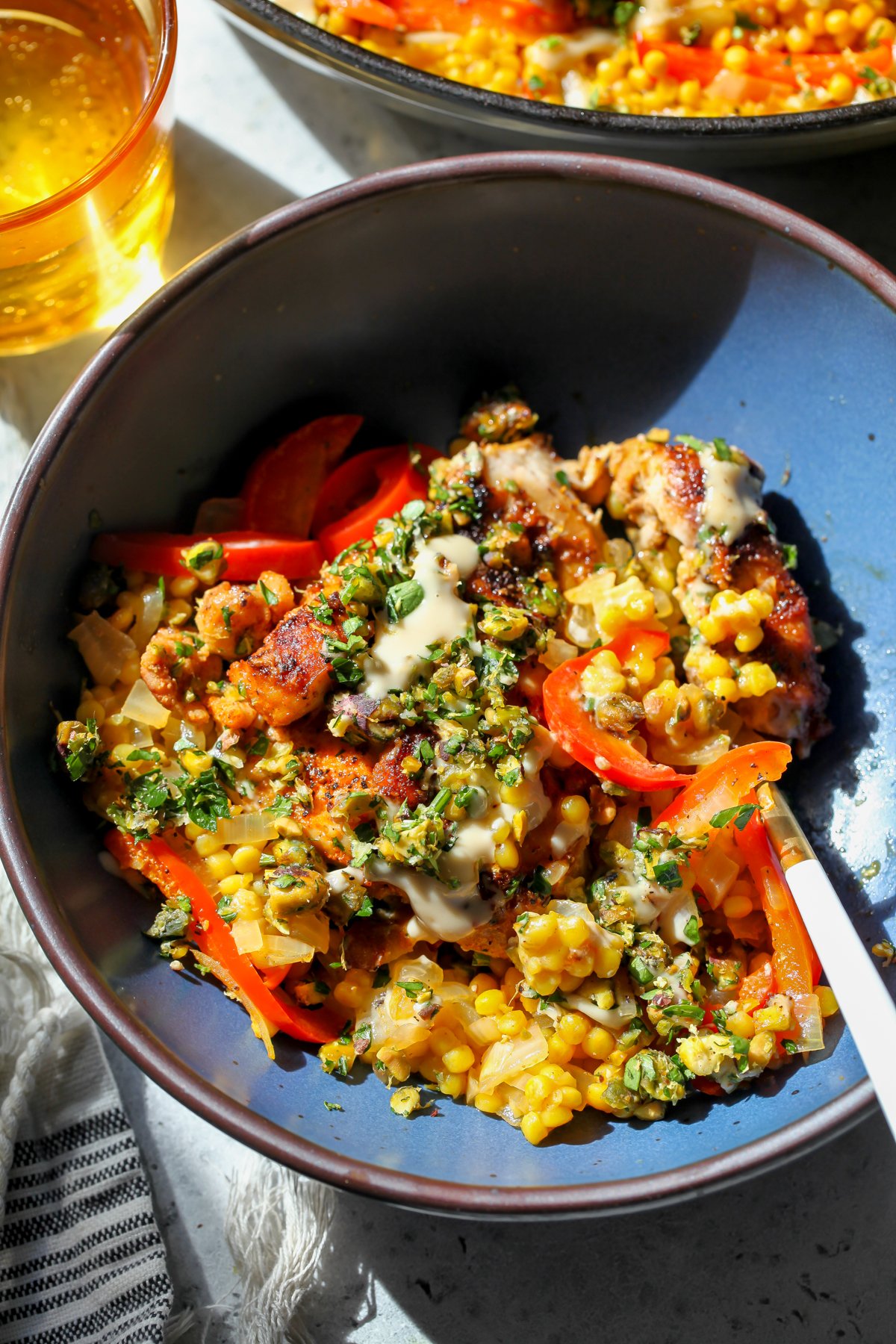 A wide-rimmed blue bowl with one serving of chicken and couscous. Fork resting on the right side of the bowl.
