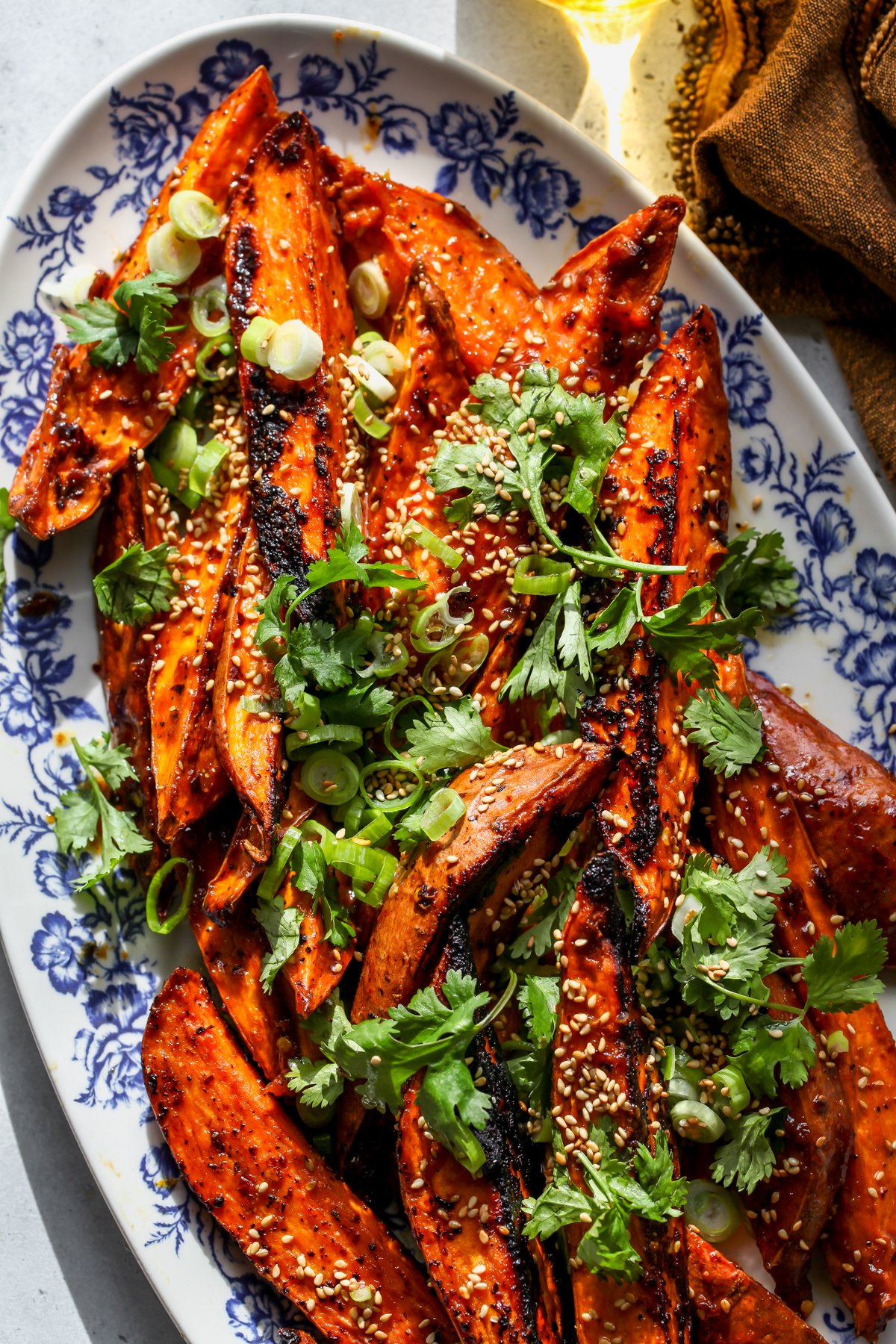 Miso-Maple Glazed Sweet Potatoes arranged on a white and blue platter topped with cilantro, scallions, and sesame seeds.