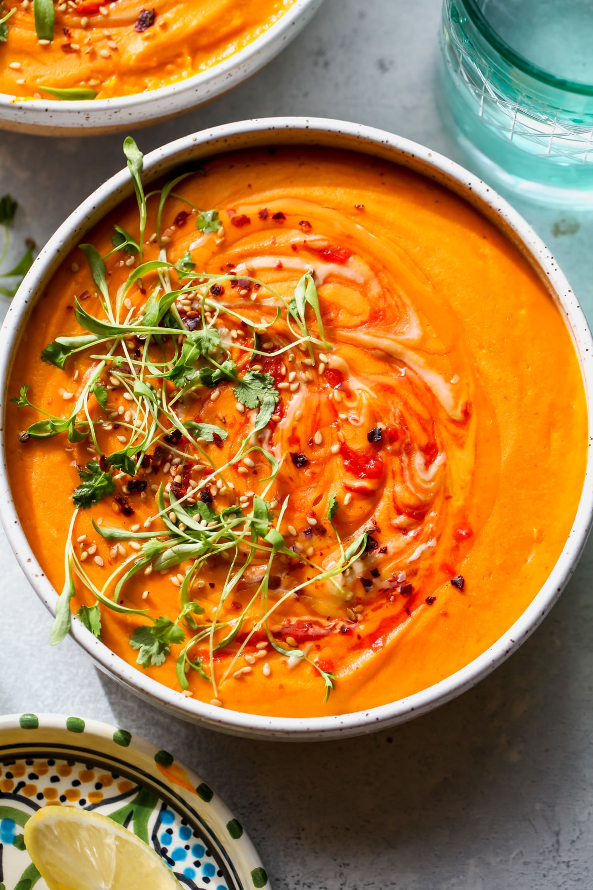 Moroccan carrot and lentil soup styled in a white bowl topped with herbs, harissa, and sesame seeds.