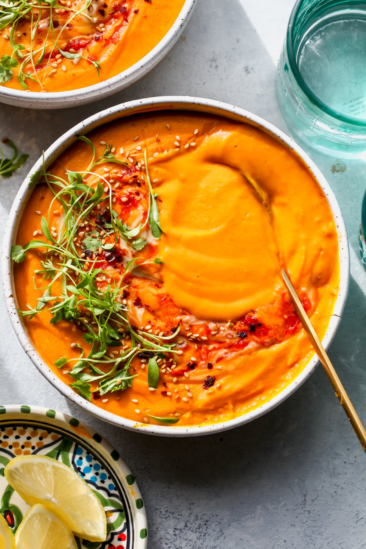 A spoon swirling carrot and lentil soup in a white bowl.