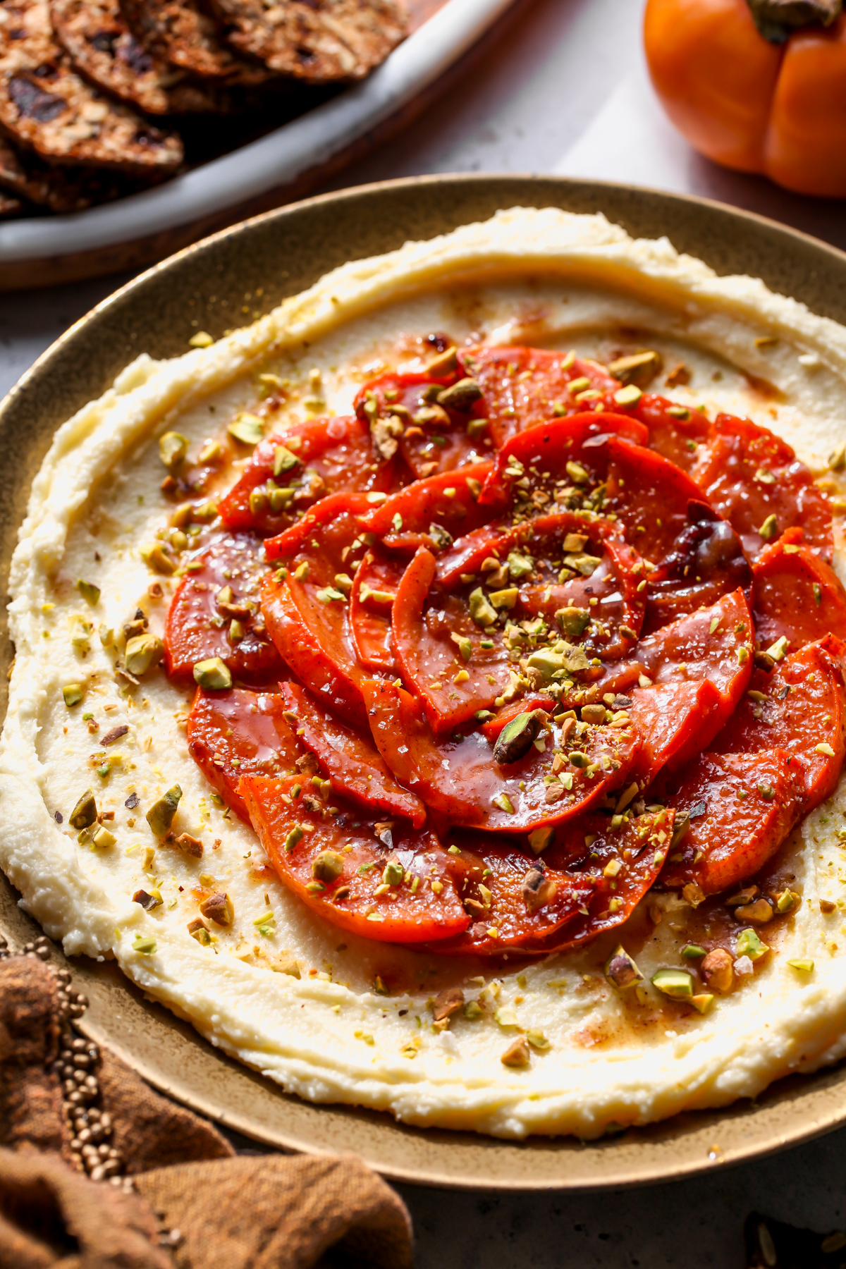 Whipped brie on a gold plate topped with caramelized persimmons and pistachios.