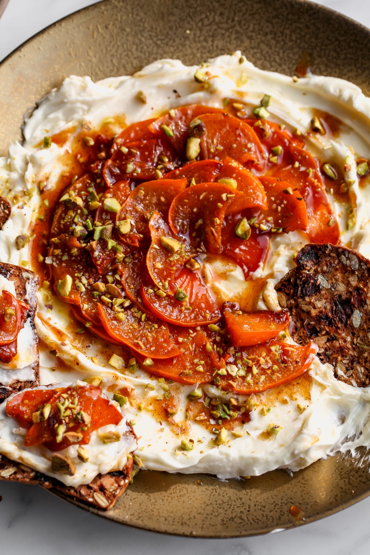 Whipped Brie with Caramelized Persimmons being dipped with crackers on a gold platter.