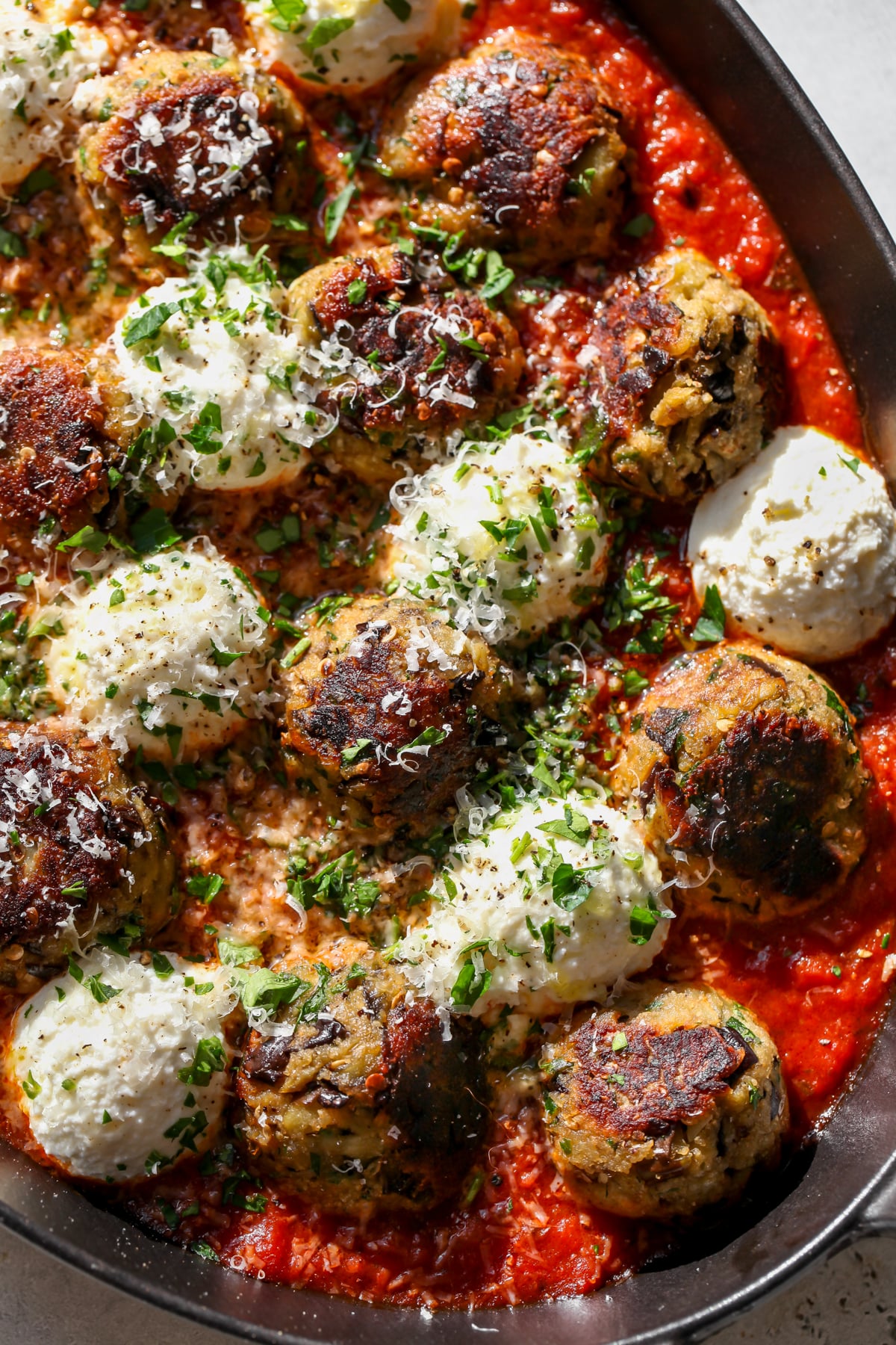 Eggplant Parmesan Meatballs styled in a pan with dollops of ricotta cheese and marinara sauce.