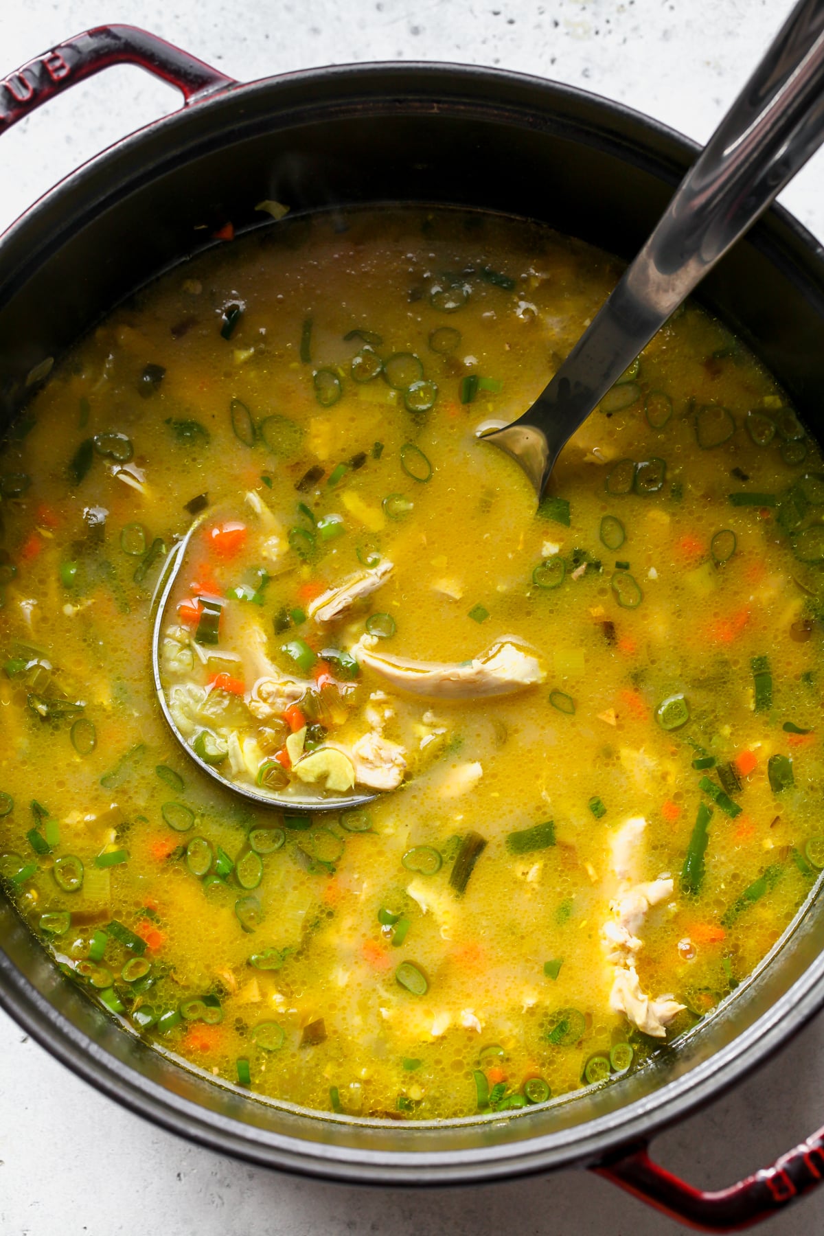 A ladle stirring chicken and rice soup in a large Dutch oven.