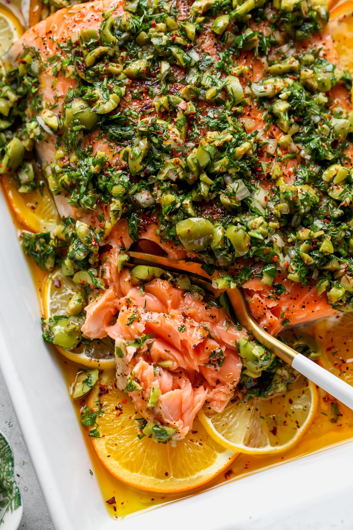 A fork flaking a piece of roasted salmon topped with olive-citrus mixture.