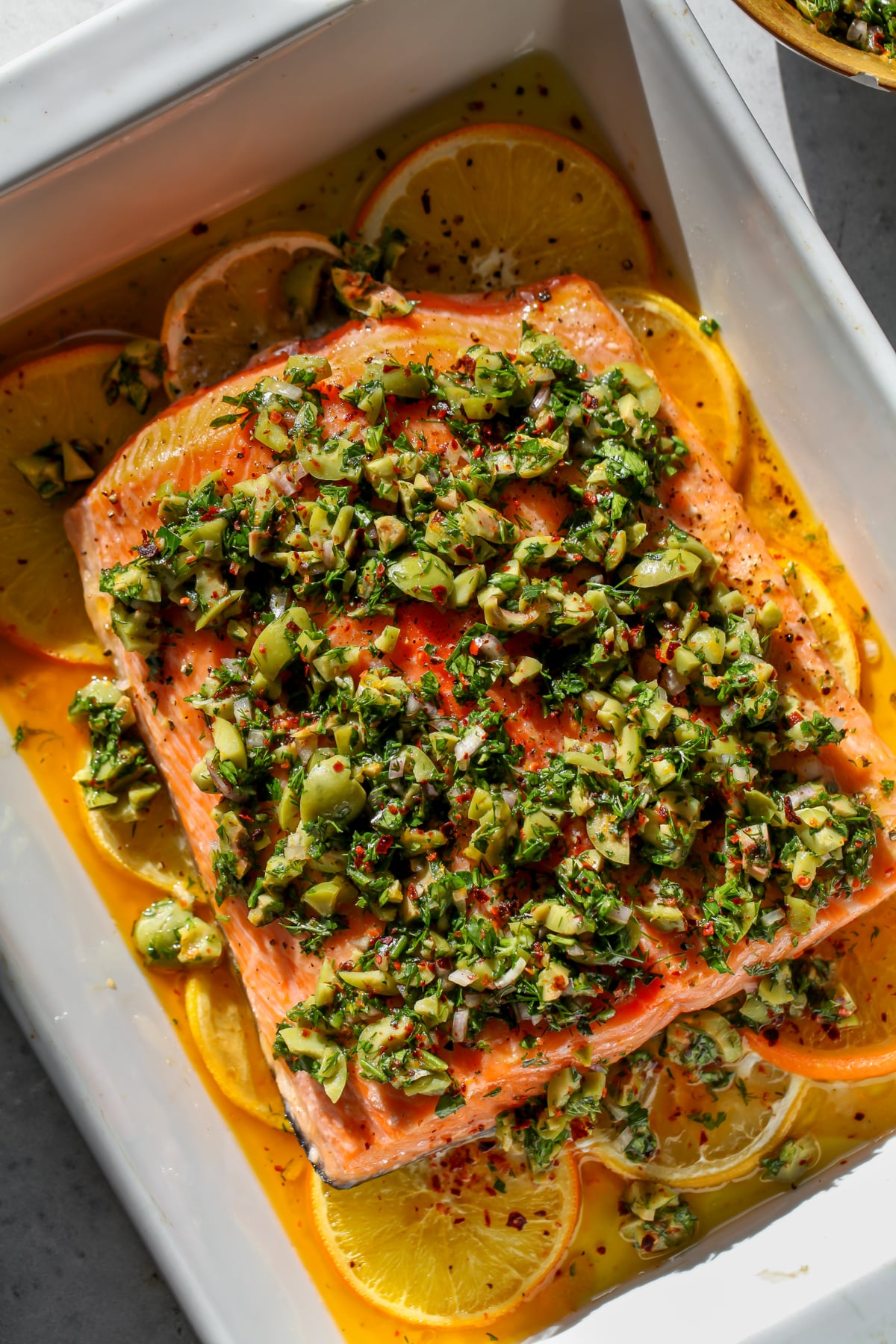 Olive-Citrus Slow Roasted Salmon arranged over citrus slices in a white baking dish.