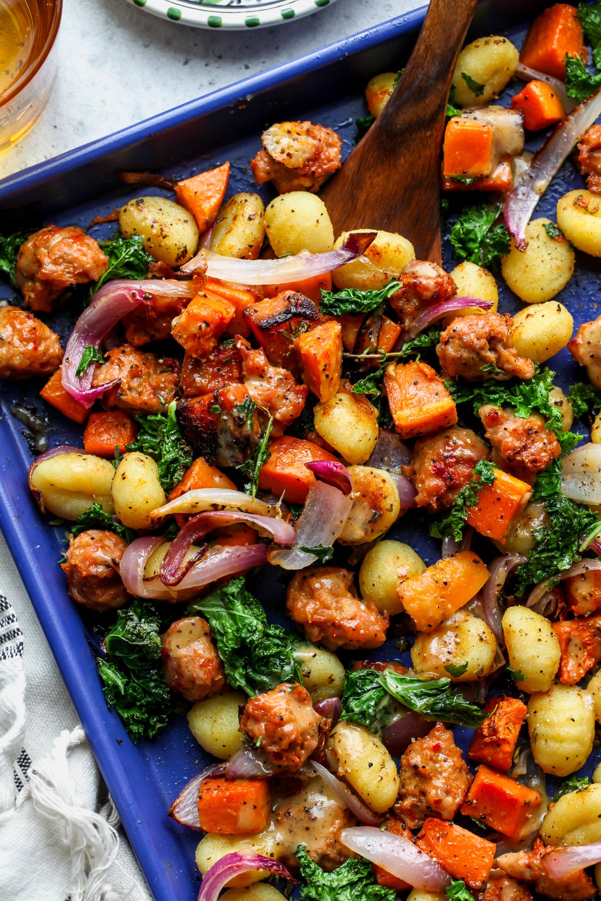 Sheet Pan Butternut Squash and Sausage Gnocchi being tossed on a blue baking sheet.