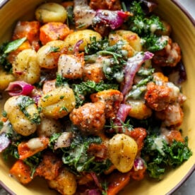 A yellow bowl filled with Sheet Pan Butternut Squash and Sausage Gnocchi and drizzled in miso sauce.