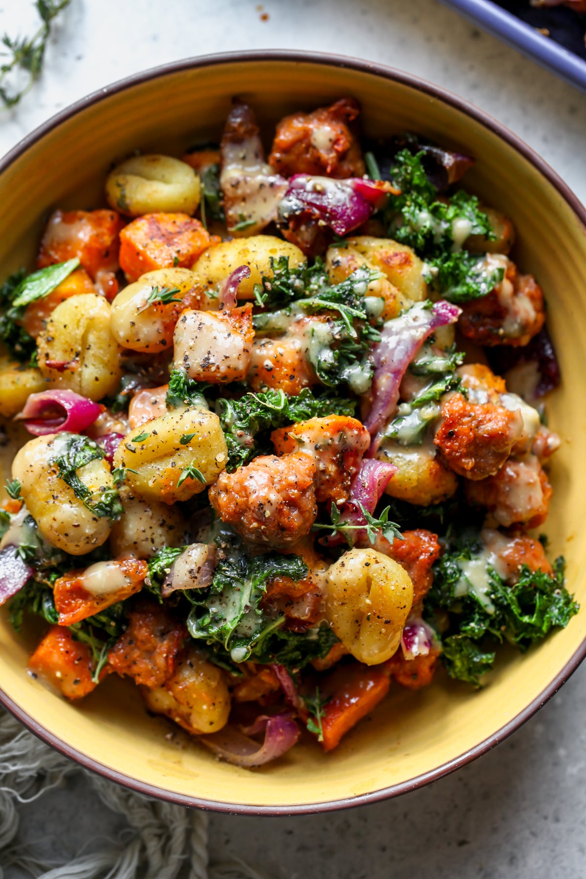 A yellow bowl filled with Sheet Pan Butternut Squash and Sausage Gnocchi and drizzled in miso sauce.