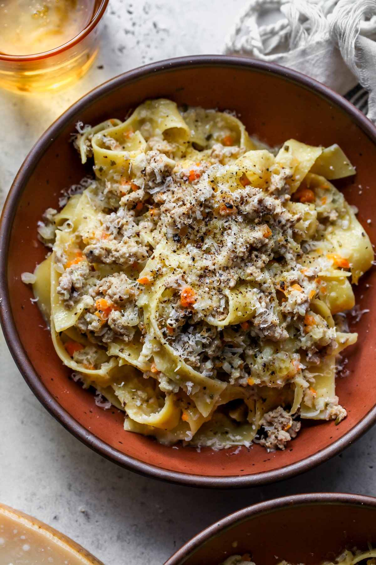 White bolognese with pappardelle styled in a maroon bowl topped with Parmesan and black pepper.