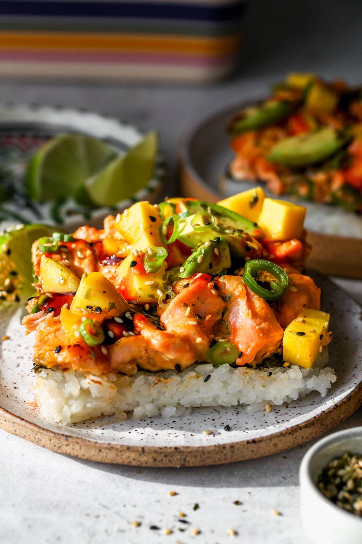 A square slice of salmon sushi bake styled on a small white speckled plate.