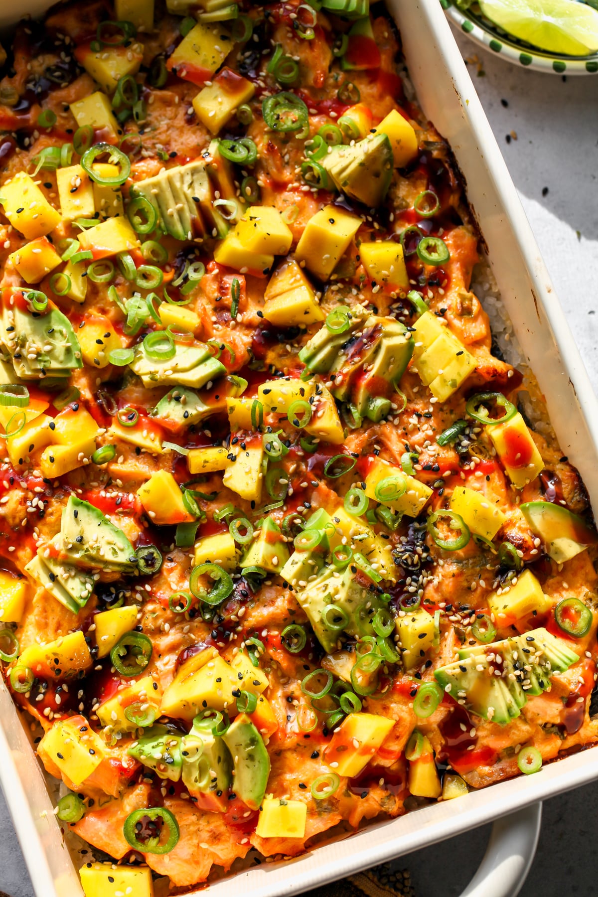 Spicy Salmon and Mango Sushi Bake with garnishes styled in a baking dish on a gray surface.