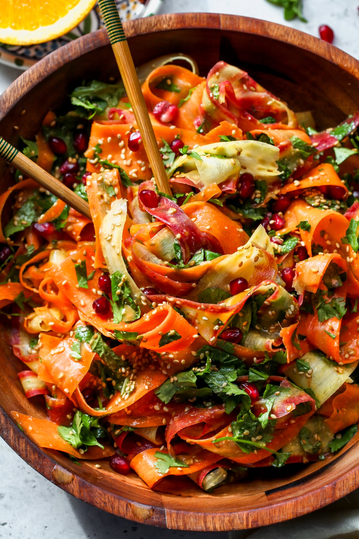 Shaved carrot salad being twirled with chopsticks in a wooden serving bowl.