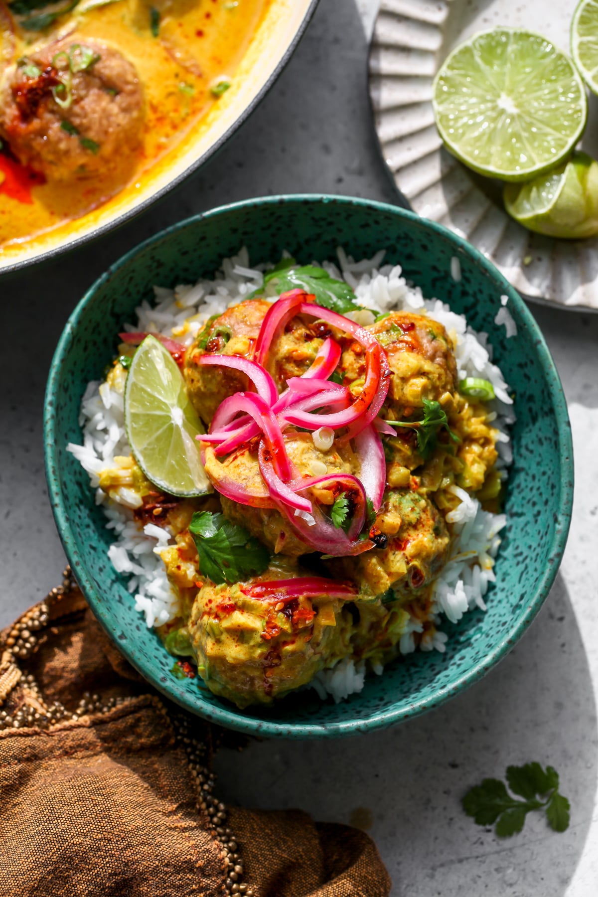 Chicken Satay Meatballs over white rice in a blue bowl topped with pickled red onion, cilantro, and chili oil.