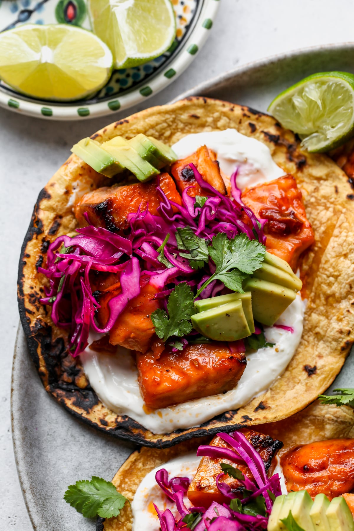 Salmon taco topped with avocado and red cabbage slaw assembled on a white plate.