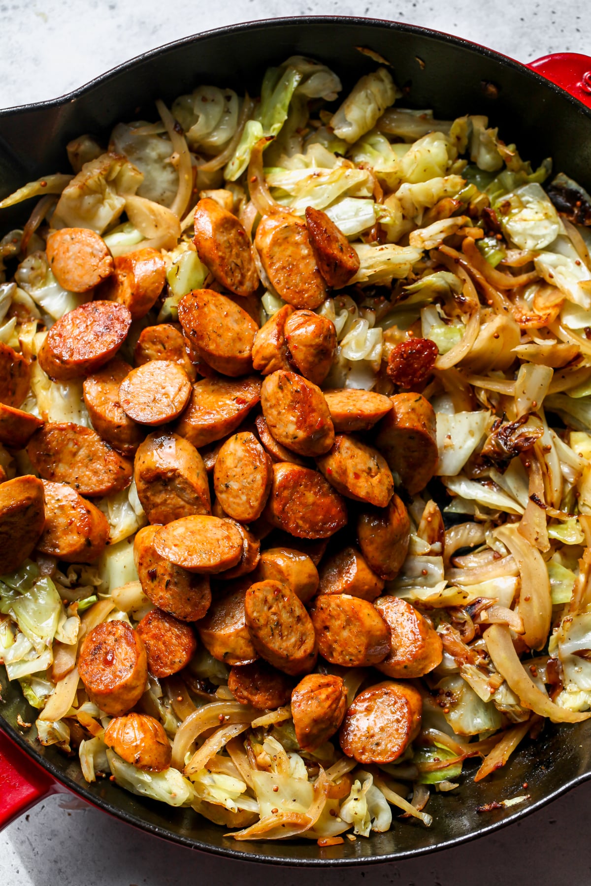 Slices of cooked chicken sausage being added to a pan of sautéed fennel and cabbage.