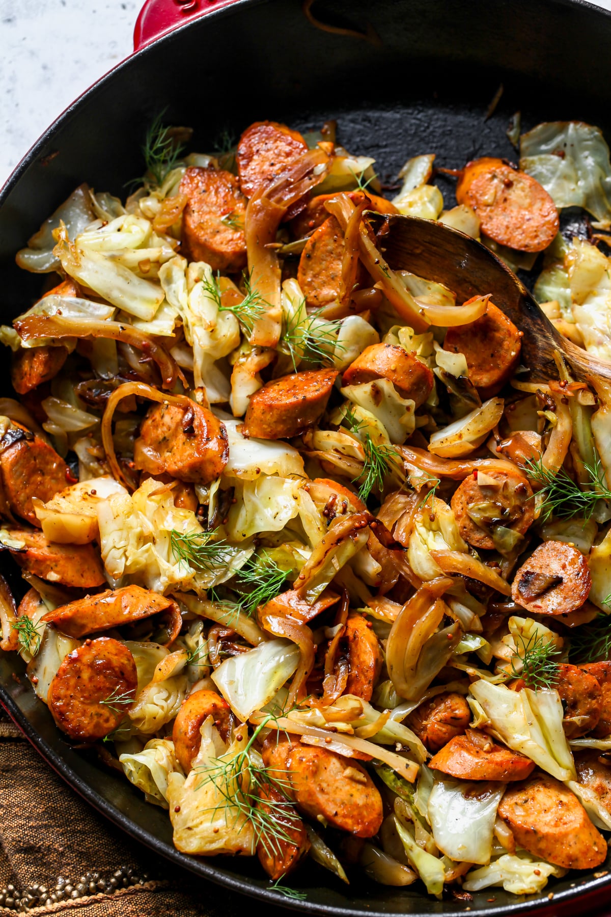 Sautéed chicken sausage and cabbage being tossed in a black cast iron skillet.