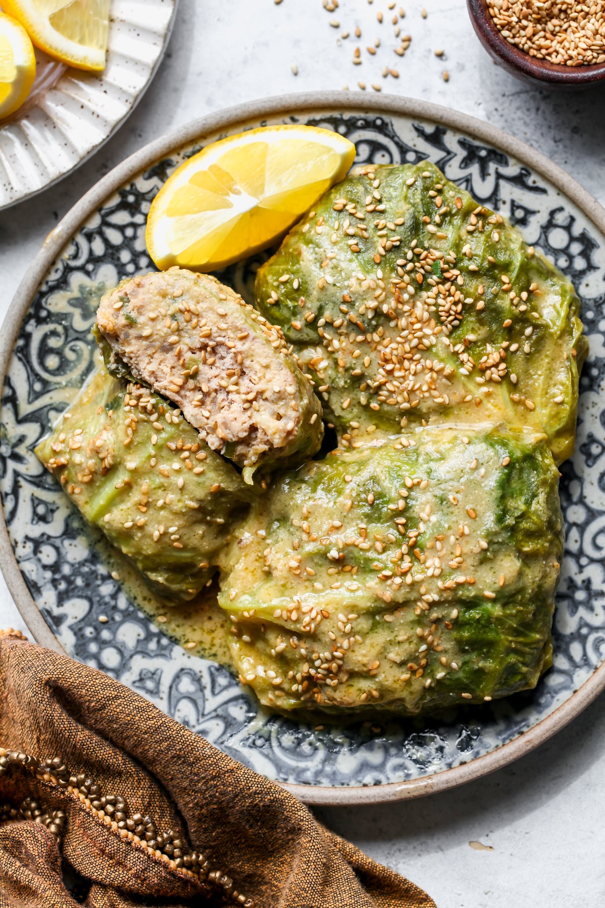 3 cabbage rolls arranged on a blue and white plate with one sliced into to show inside filling.