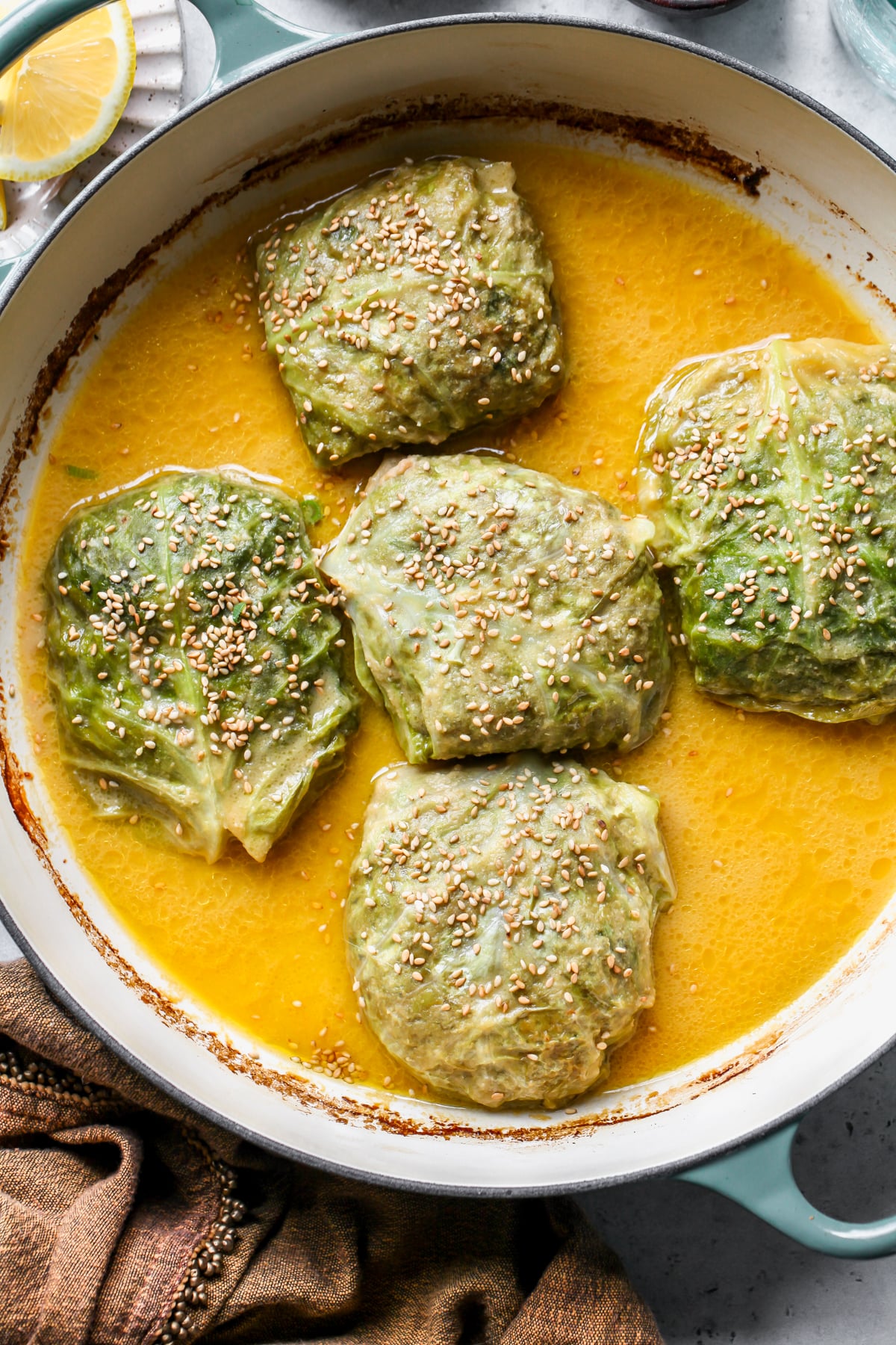 5 braised cabbage rolls in miso butter sauce arranged in a large sauté pan after baking.