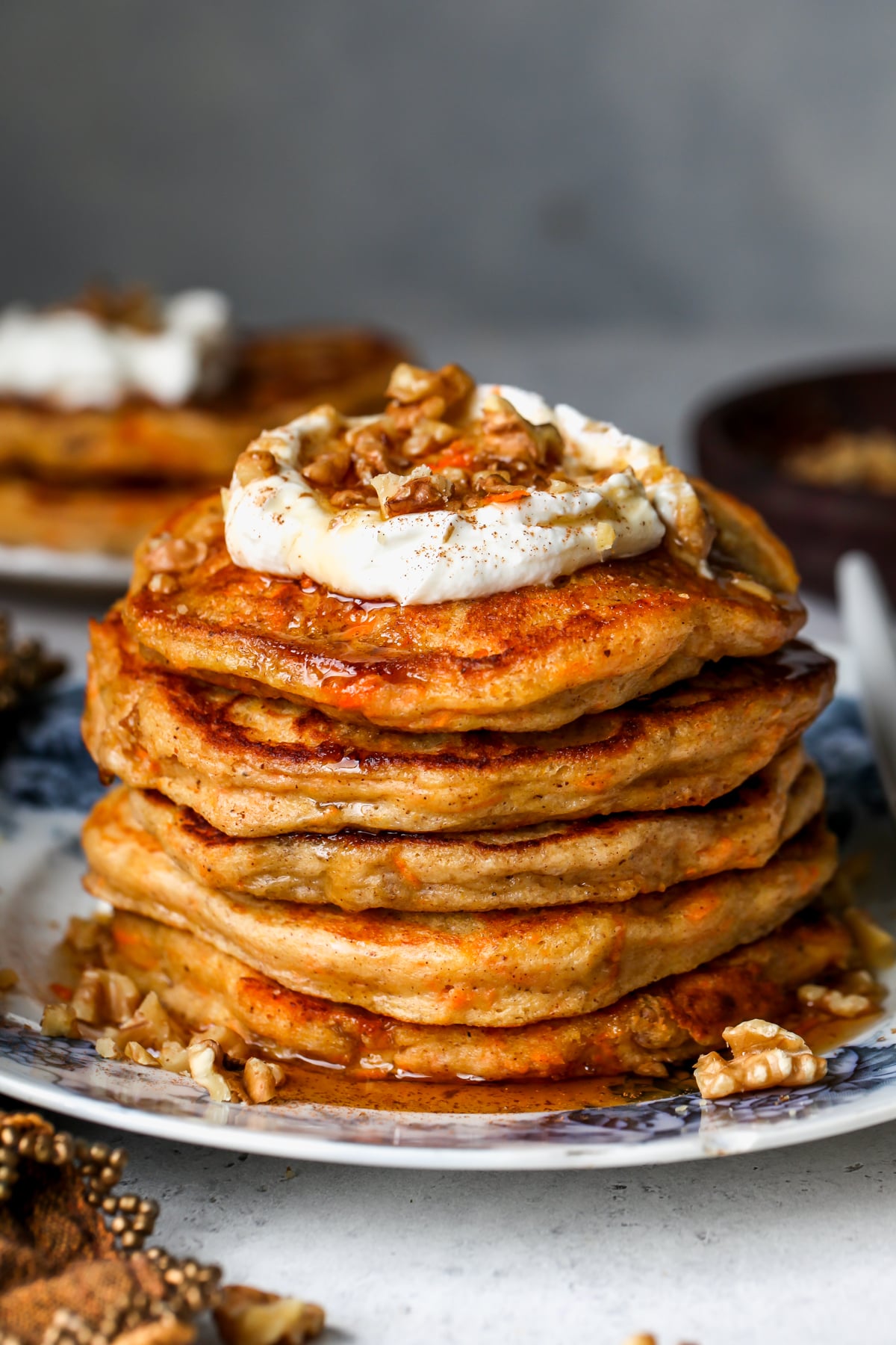 A stack of carrot cake pancakes topped with Greek yogurt, walnuts, and maple syrup on a blue and white floral plate.