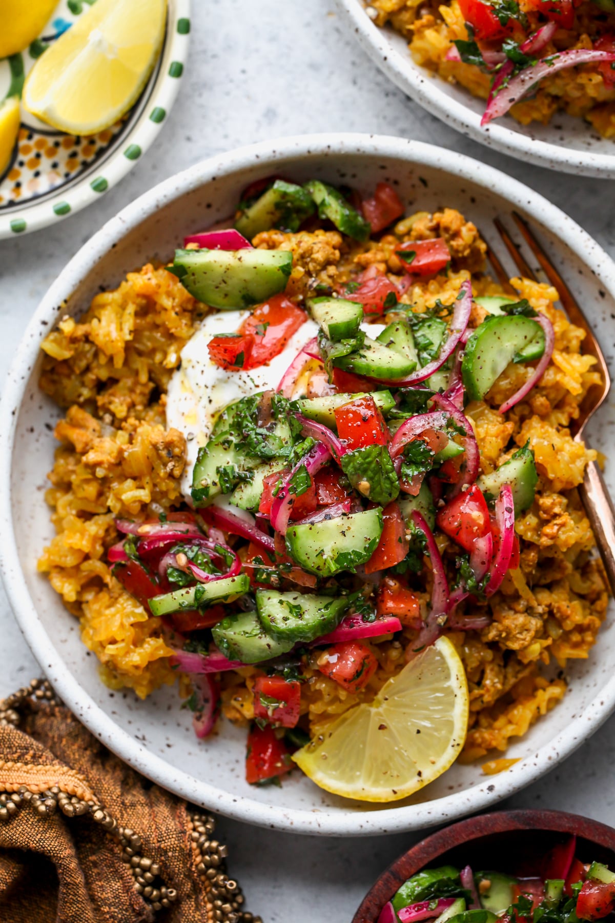 Ground turkey and rice mixture in a white bowl topped with a dollop of yogurt and sumac-cucumber salad.