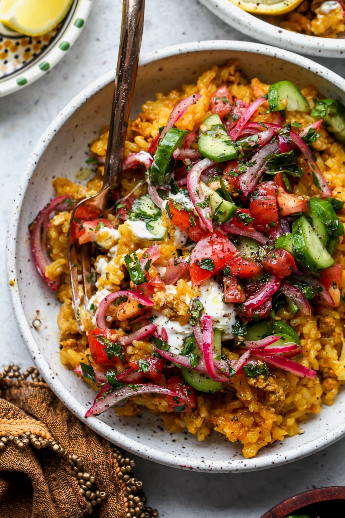A fork mixing turkey and rice mixture with yogurt and cucumber salad topping in a white bowl.