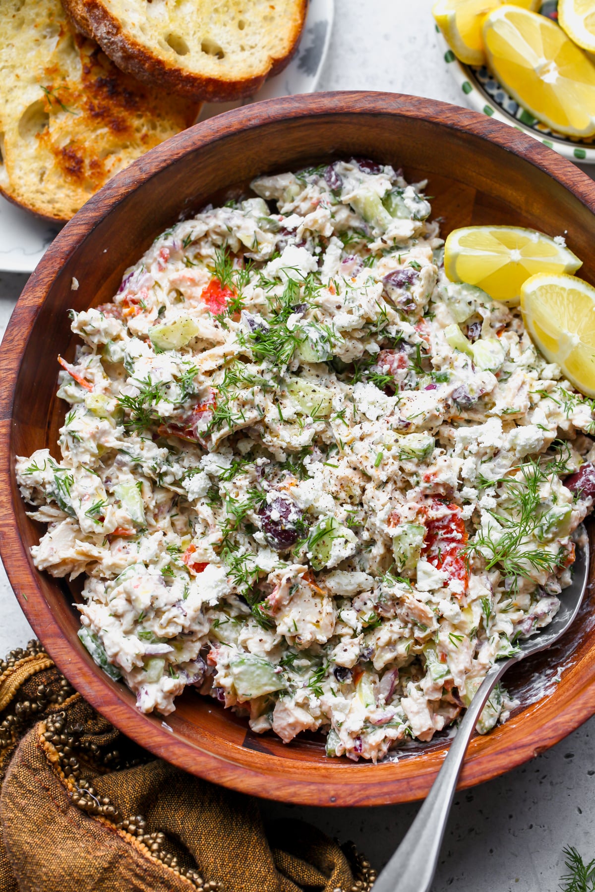 Greek chicken salad in a large wooden serving bowl topped with fresh dill.
