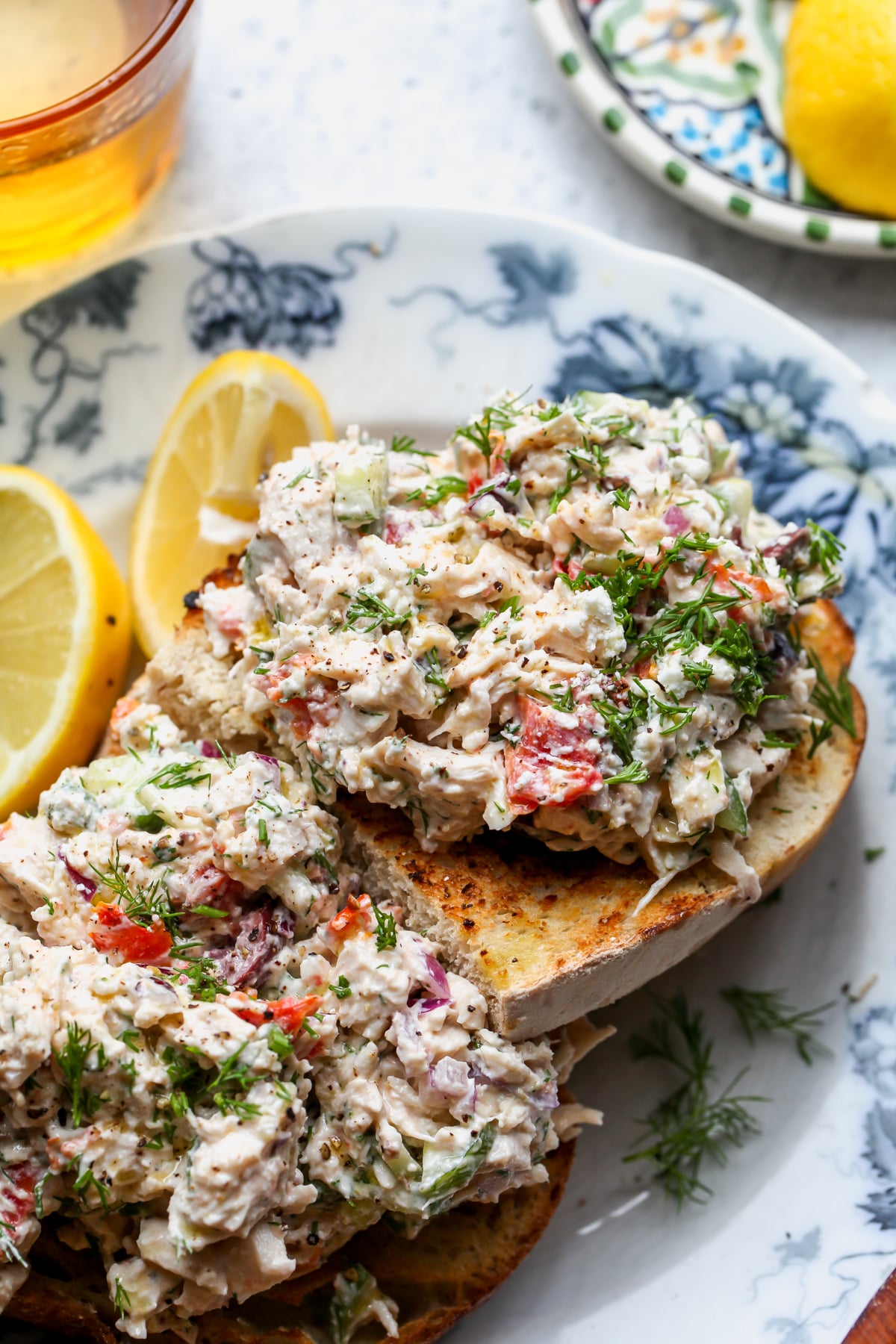 Greek Chicken Salad on a slice of toasted sourdough bread on a blue and white floral plate.
