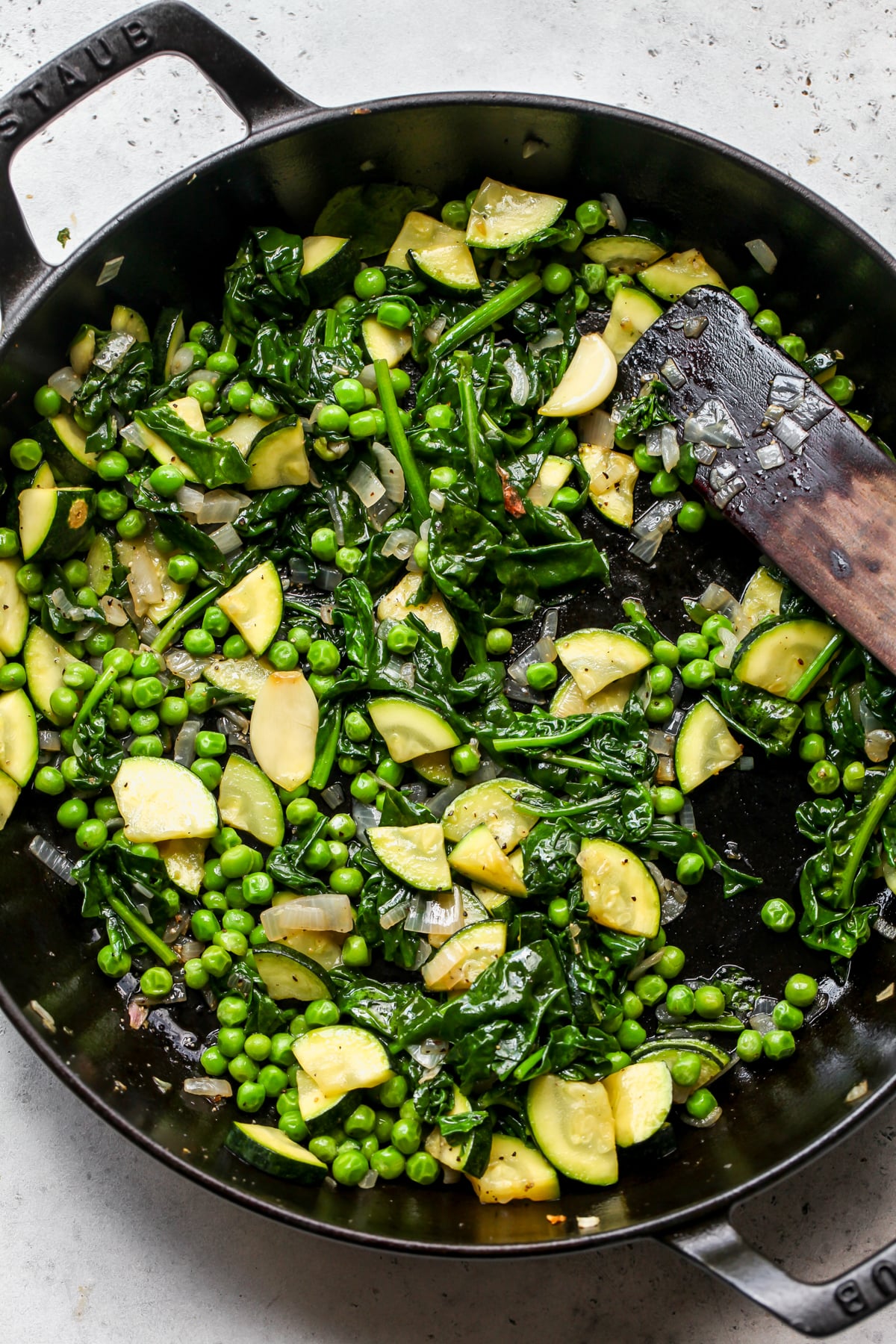 Veggies and aromatics being sautéed in a large cast iron skillet.