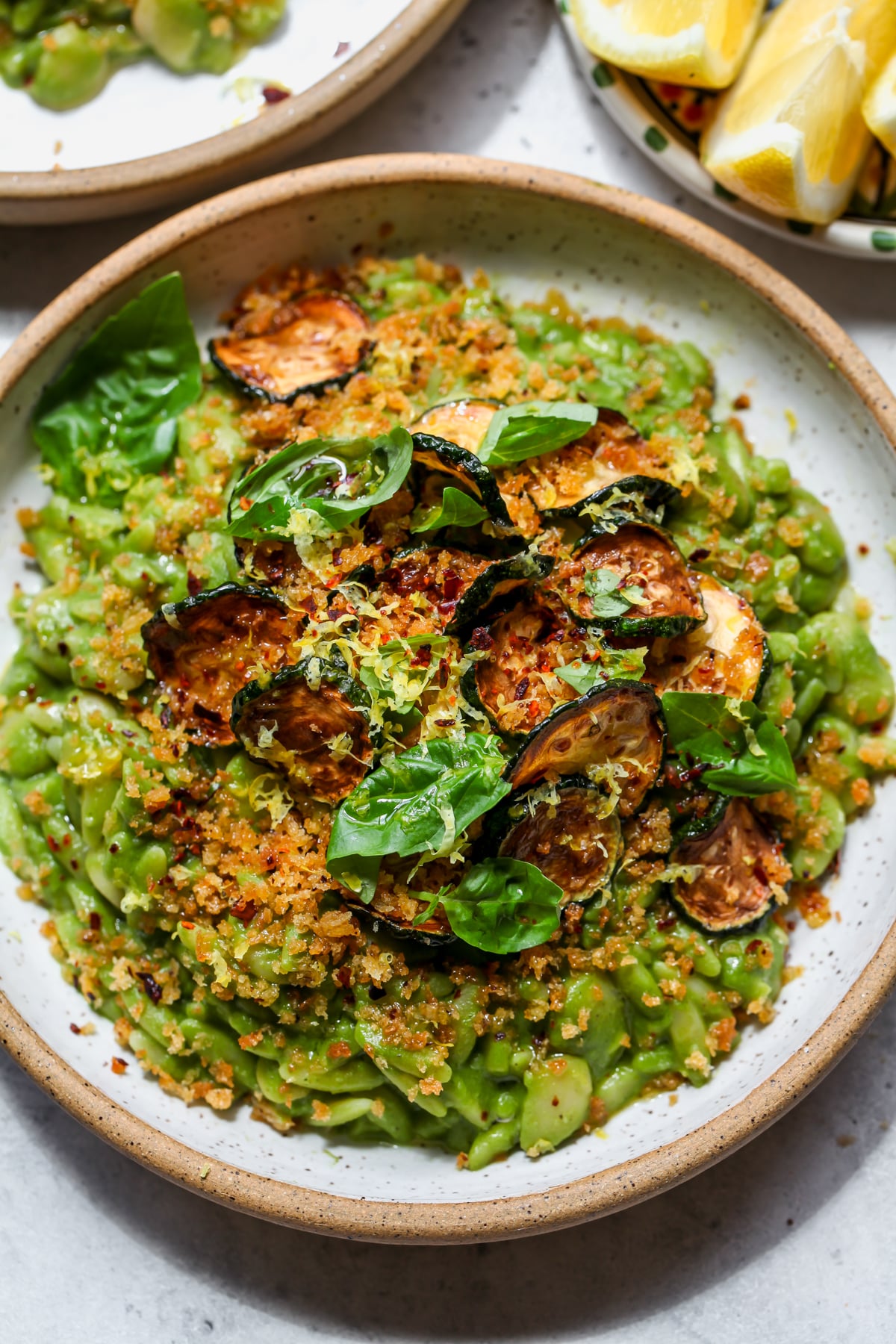 Green Goddess Butter Bean Orzo styled in a white bowl topped with fried zucchini, panko, and lemon zest.