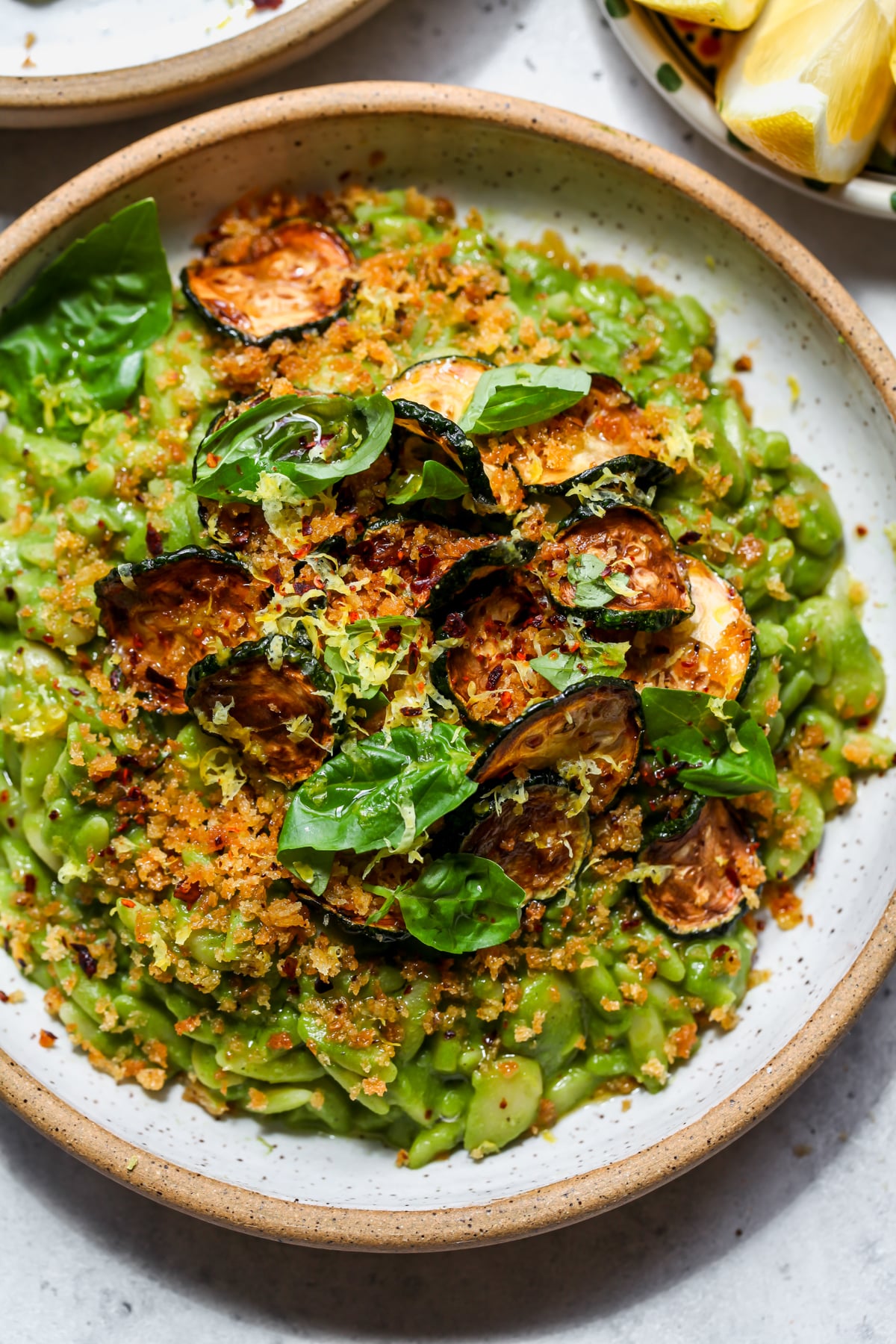 Vegan green goddess orzo styled in a white bowl topped with crispy panko, zucchini, and basil leaves.