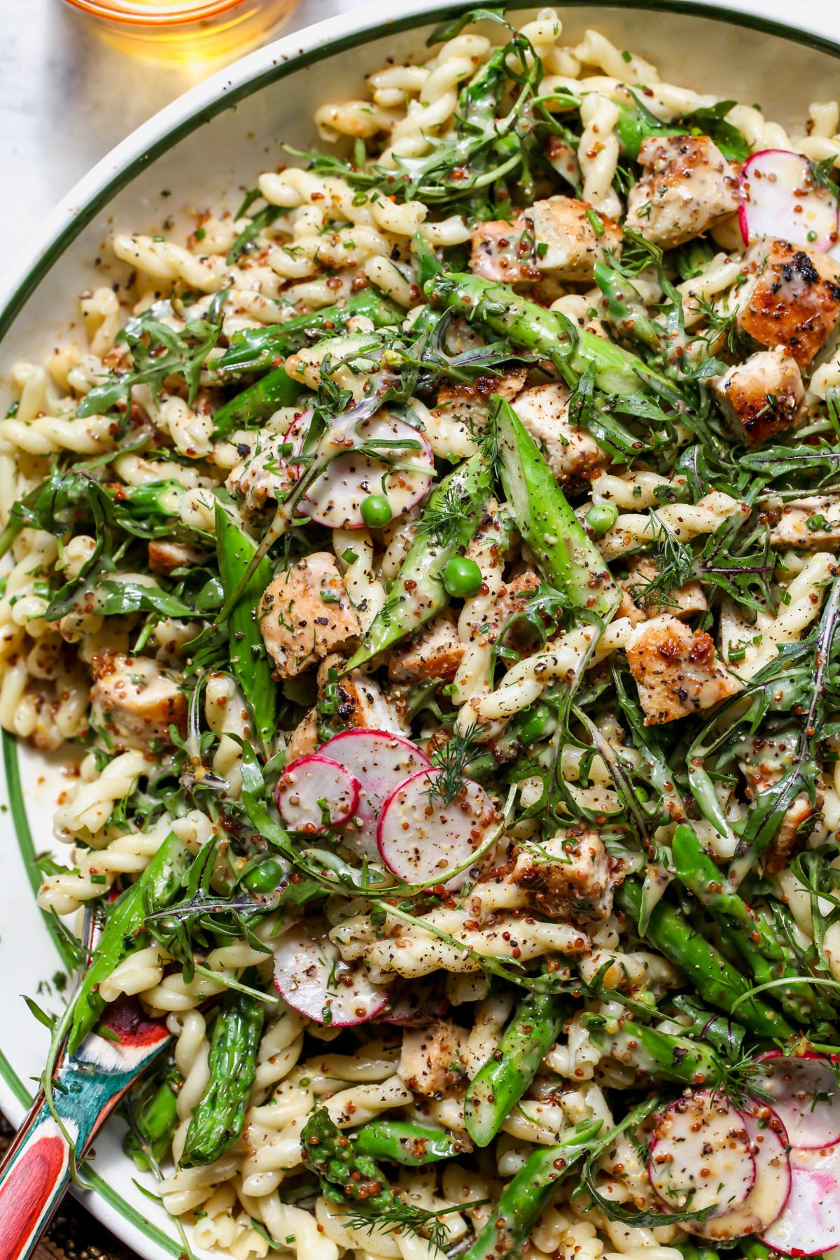 Honey Mustard Chicken Pasta Salad being tossed in a large white mixing bowl.