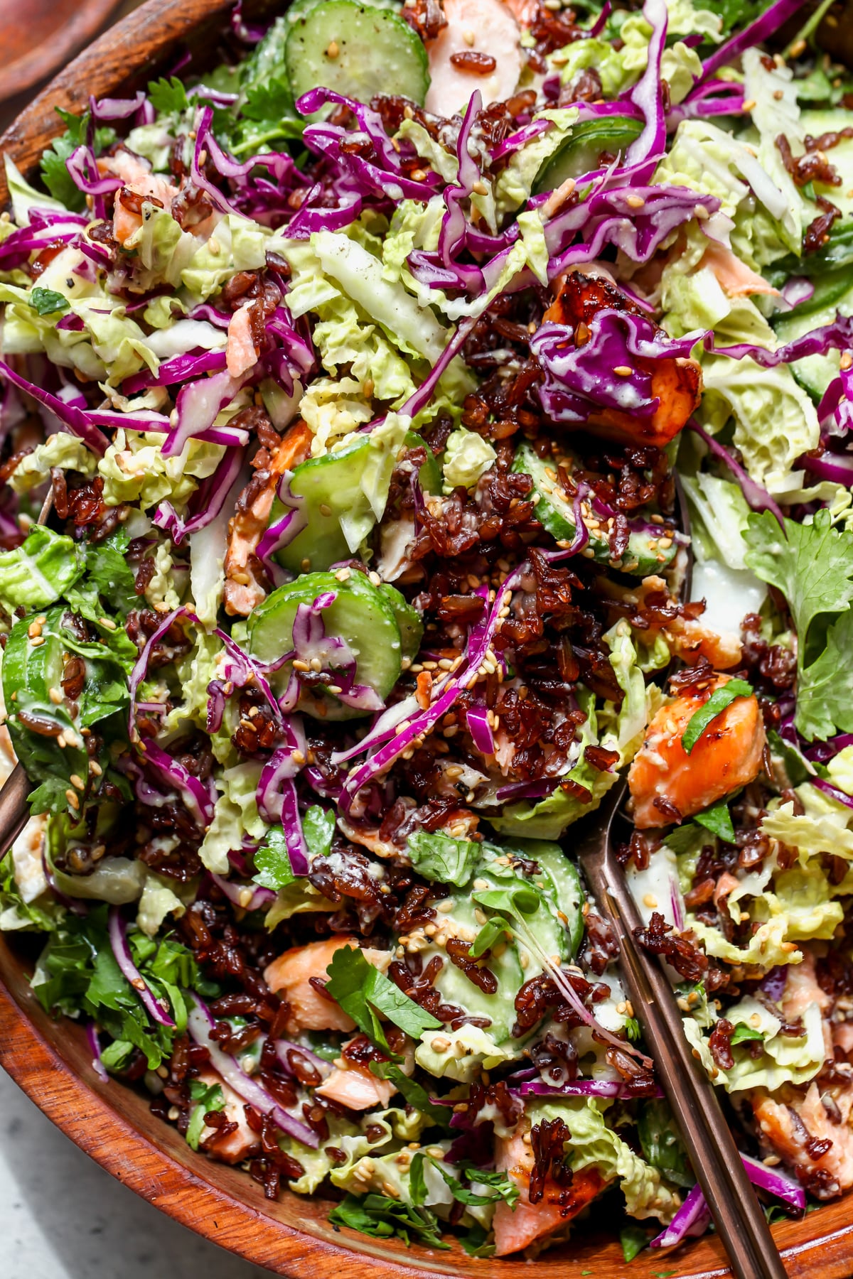 Salmon Crispy Rice Salad being tossed in a wooden serving bowl.