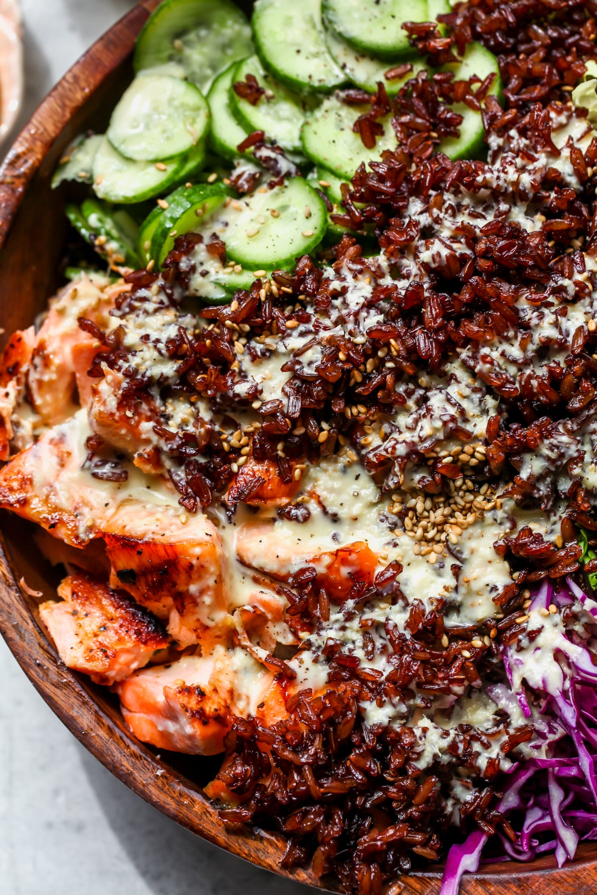 Crispy rice and dressing being added to a salmon and cabbage salad in a wooden bowl.