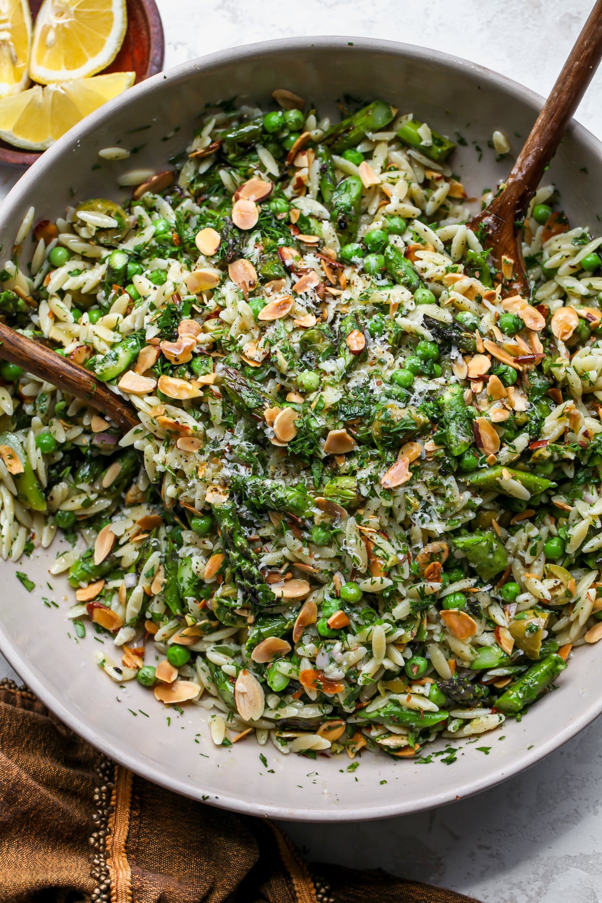 Asparagus Orzo Pasta Salad being tossed with serving utensils in a large tan salad bowl.