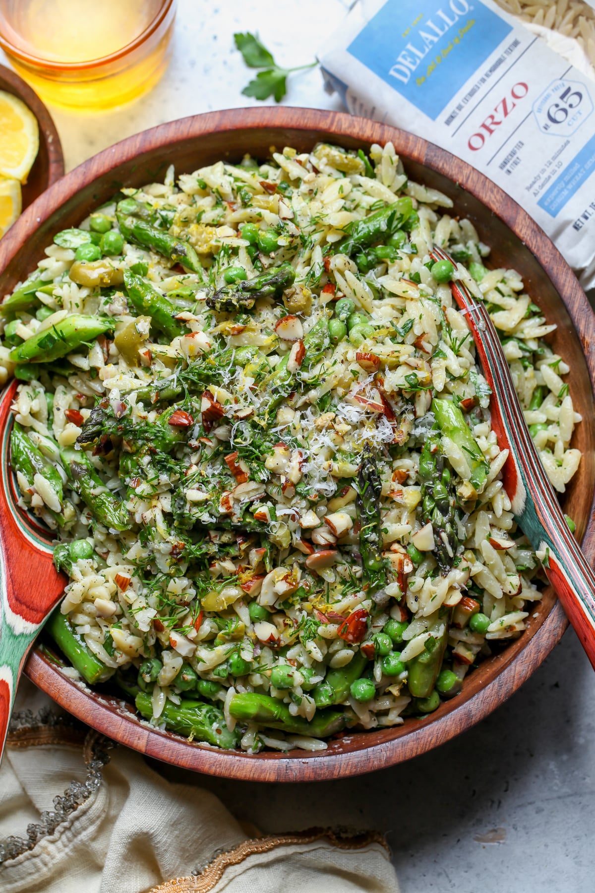 Asparagus pasta salad topped with fresh herbs and toasted almonds assembled in a large wooden serving bowl.