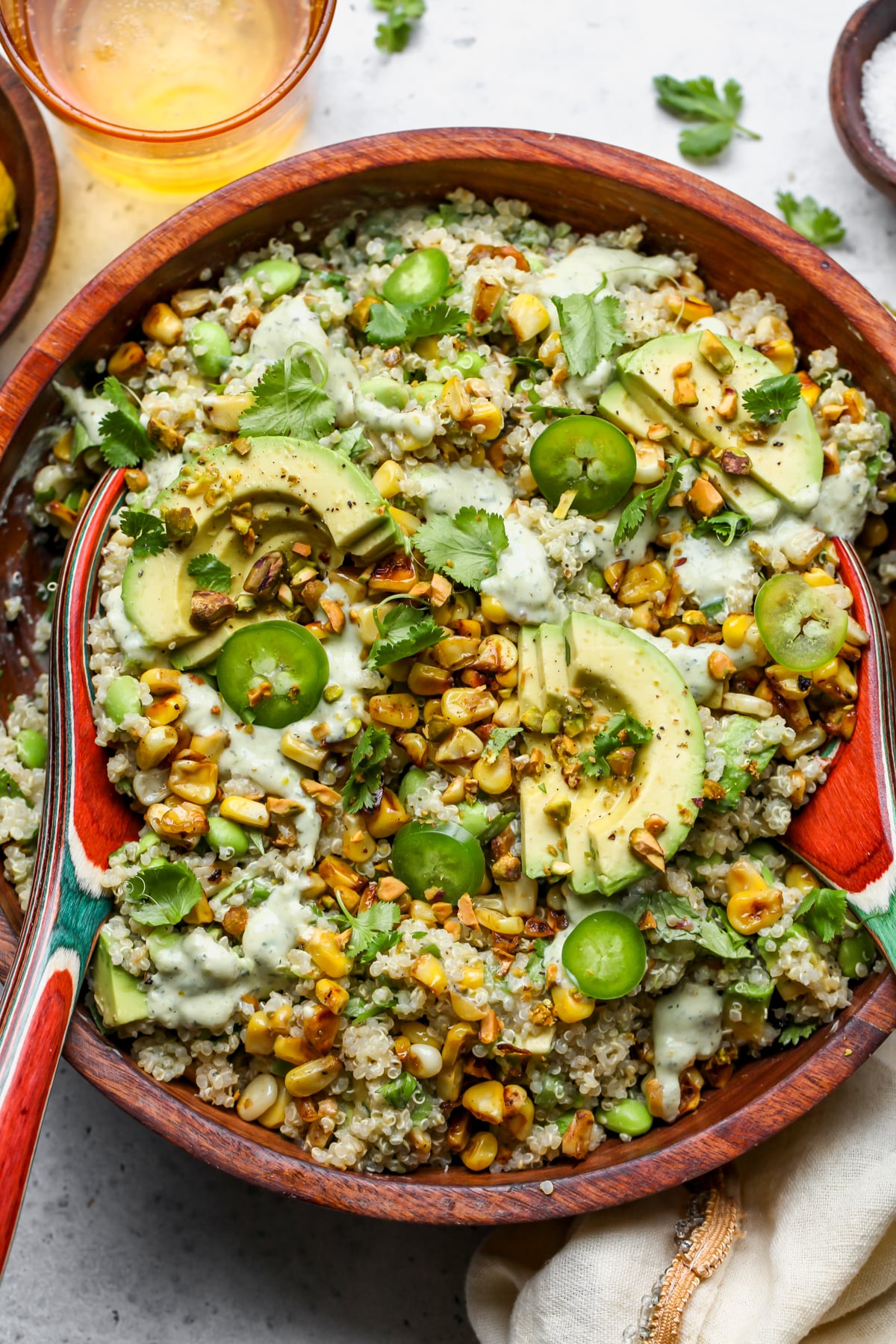 Charred Corn and Edamame Quinoa Salad topped with avocado, herbs, and pistachios styled in a wooden serving bowl.