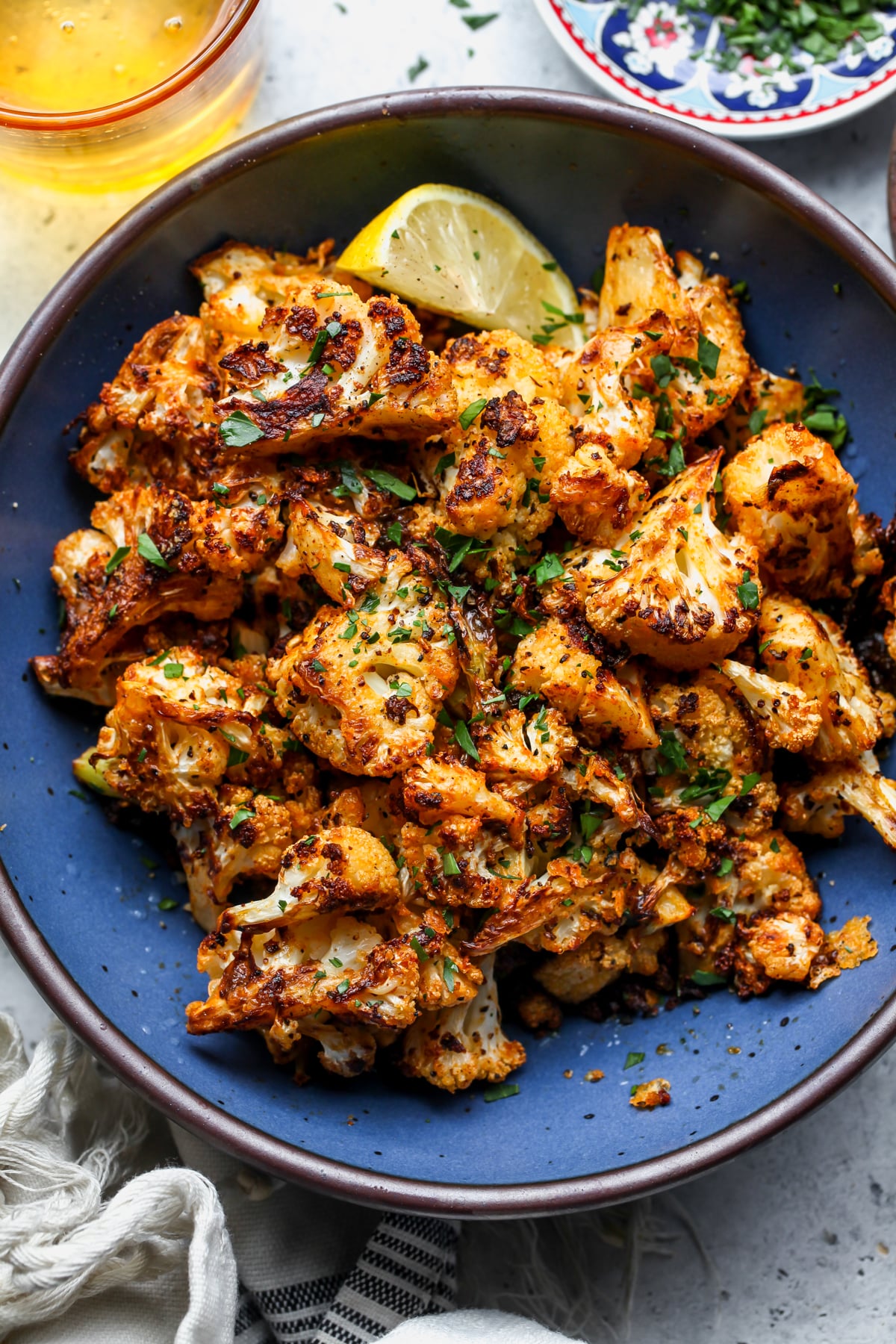 Roasted Cauliflower topped with parsley and lemon juice styled in a dark blue round serving bowl.