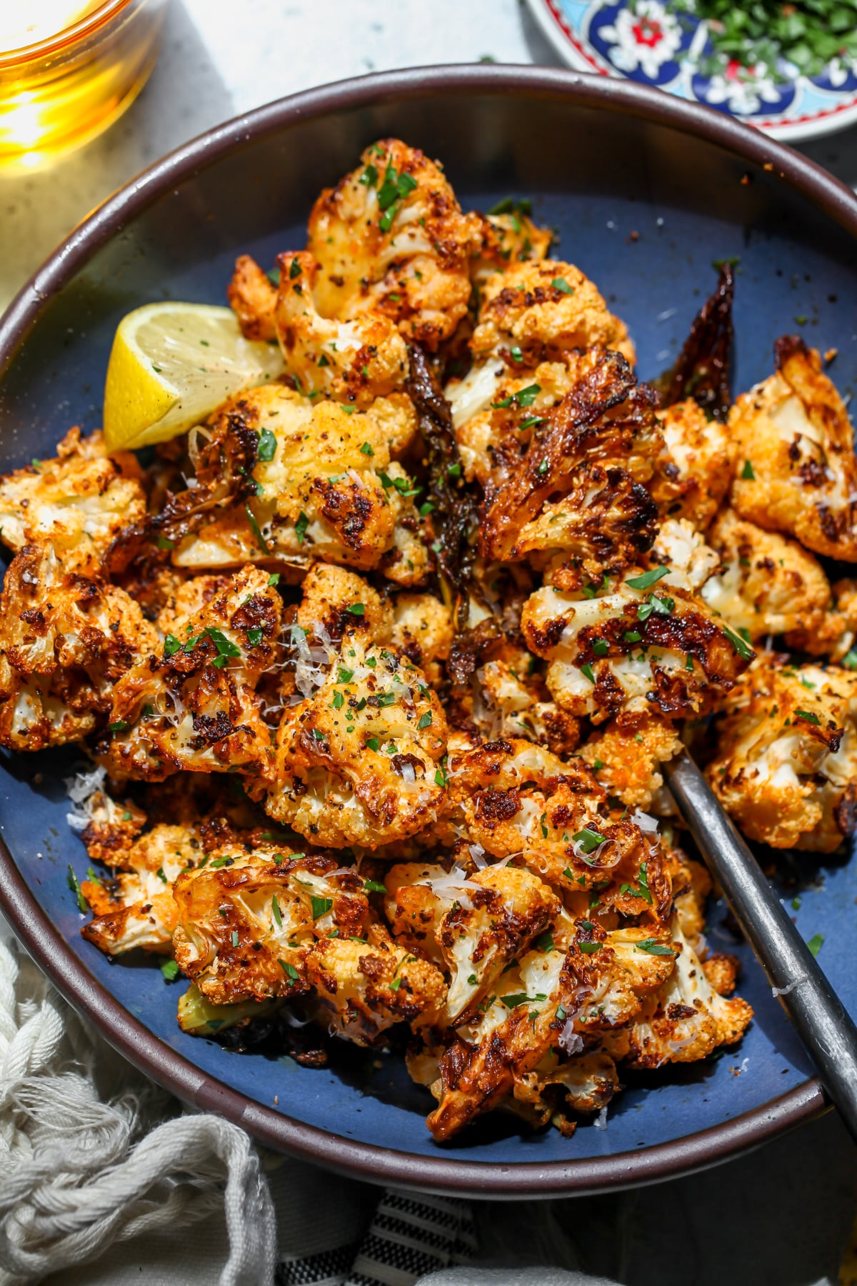 Garlic-Parmesan Roasted Cauliflower styled in a blue serving bowl with a lemon wedge on the left side.