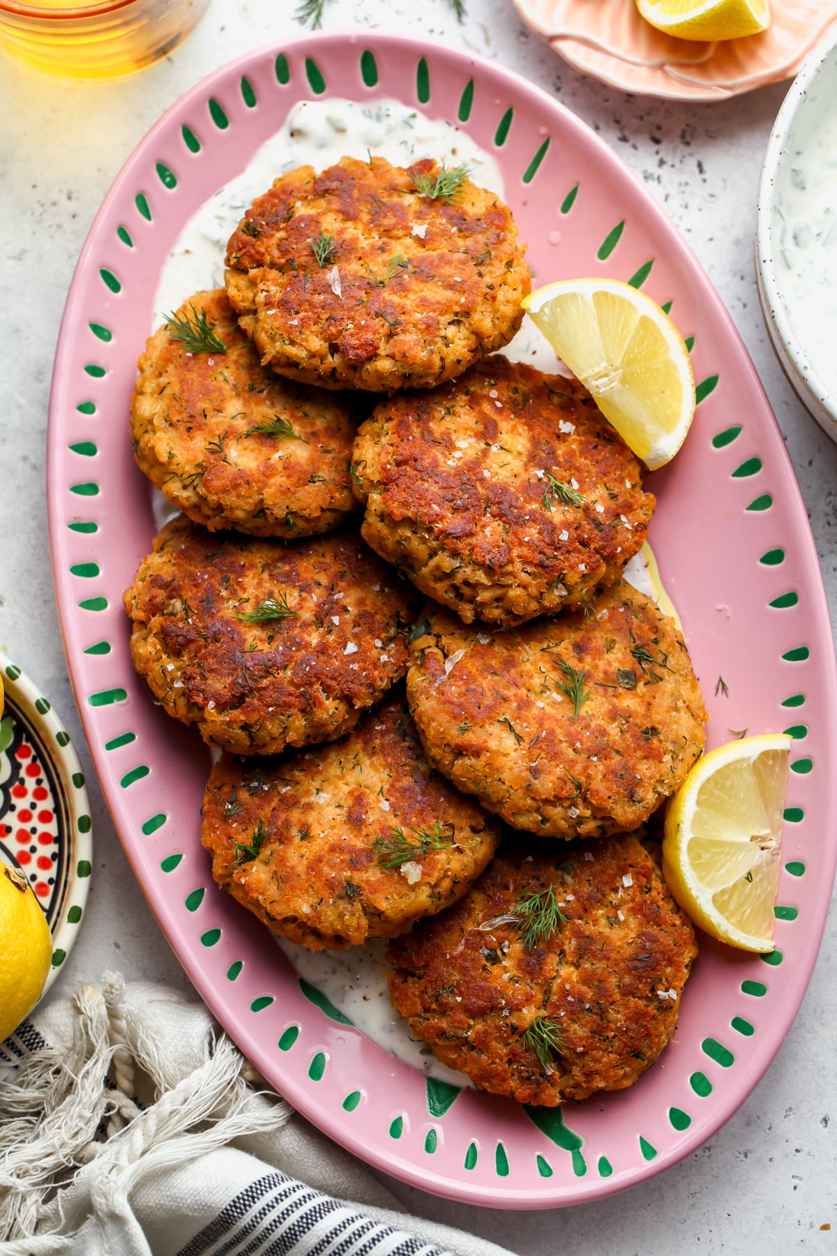 Canned salmon patties served over tartar sauce on a large oval pink serving platter.