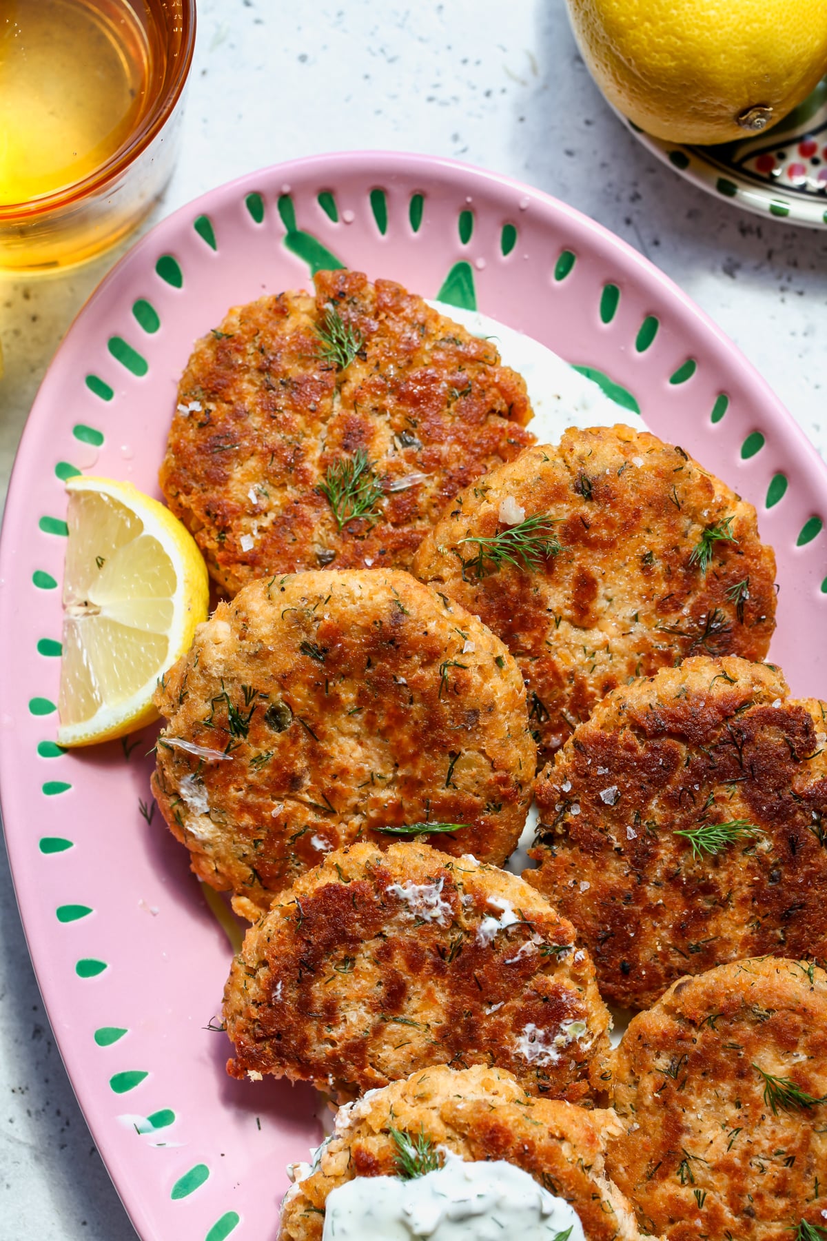 Easy Canned Salmon Patties arranged on a pink platter with tarter sauce and lemon wedges.